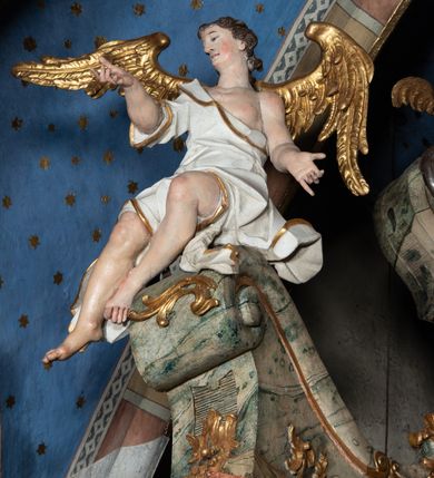 Zdjęcie nr 39: Ołtarz architektoniczny, trójosiowy, z wydzieloną częścią cokołową z bramkami bocznymi, jednokondygnacyjny, ze zwieńczeniem. Mensa drewniana z portatylem z marmuru dębnickiego, umieszczona na drewnianej, prostopadłościennej skrzyni.  Antepedium w kształcie leżącego prostokąta, ujęte profilowaną ramą dekorowaną liśćmi akantu i perełkowaniem. W polu płaskorzeźbione przedstawienie baranka leżącego na krzyżu, na obłoku, ujęte parą liści akantu oraz wicią roślinną z kwiatami i kiściami winogron. 
Na mensie tabernakulum z Tronem Łaski w formie prostopadłościanu na cokole, o wypukłej ściance frontowej, ujęte spływami wolutowymi podtrzymującymi niepełne belkowanie, wyłamane po środku łukiem półkolistym. Na froncie obrotowa nisza ujęta obramieniem w kształcie stojącego prostokąta zamkniętego łukiem nadwieszonym. W niszy ryte przedstawienie kielicha z Eucharystią w glorii, na obłoku, całość w rocaillowej ramie. Powyżej tron wystawienia z cokołem dekorowanym rocaille’em i parą ornamentalnych świeczników; ujęty parą kolumn dźwigających imposty. Podpory dżwigają rocaillowe kabłąki tworzące baldachim, na którego szczycie figurka baranka eucharystycznego leżącego na księdze. Ścianka w formie zbliżonej do stojącego prostokąta ujęta rocaille. Tabernakulum i tron ujęte okazałymi spływami wolutowymi z rocaillowymi uszami oraz na zakończeniach u dołu dwiema rzeźbami klęczących, adorujących aniołów.
Osie nastawy wydzielone w osiach skrajnych parą kolumn o skręconych trzonach i korynckich kapitelach umieszczonych na tle pilastrów, w osiach wewnętrznych parą pilastrów o trzonach w formie wolut z puttami z puttami, podtrzymywaną przez kariatydy w formie okazałych figur uskrzydlonych aniołów. Podpory wspierają pełne belkowanie z profilowanym gzymsem, występujące nad nimi, przerwane nad polem środkowym. W polu środkowym nisza ze sklepieniem kolebkowym wspartym na dwóch filarach i pilastrach. W głębi niszy obraz Św. Bartłomiej w profilowanej ramie w kształcie stojącego prostokąta zamkniętego łukiem odcinkowym. Na podniebiu niszy obraz Męczeństwo św. Bartłomieja w kształcie leżącego prostokąta ujętego niesymetrycznym obramieniem z motywem rocaille’ów. Nisza flankowana z figurami św. Stefana i św. Emeryka umieszczonymi na konsolach, na tle pilastrów. Pola retabulum w osiach skrajnych wklęsłe, między podporami prześwity z figurami św. Piotra i św. Pawła. W partii wysokiego cokołu bramki ujęte od zewnątrz wklęsłymi filarami podtrzymującymi belkowanie, wejścia z drzwiczkami w kształcie stojącego prostokąta zamkniętego łukiem półkolistym z obrazami przedstawiającymi Mojżesza i Aarona. Zwieńczenie w formie aedikuli ujętej pilastrami wspierającymi przerwane belkowanie oraz fantazyjnymi spływami wolutowymi, spływającymi na wewnętrzne podpory, przyjmując formę przerwanego przyczółka, na którym dwa putta i dwie figury siedzących aniołów. W osiach zewnętrznych podpór dwa putta siedzące kanelowanych postumentach i obłokach, prawe przytrzymuje skórę (atrybut św. Bartłomieja). W polu zwieńczenia obraz Św. Anna Samotrzeć w kształcie wydłużonego ośmioboku, w ornamentalnej ramie. Całość zwieńczona rzeźbioną półpostacią Boga Ojca pośród obłoków ukazanego w glorii promienistej. Drzwi do bramek flankowane liściastymi festonami, powyżej tarcze ujęte liśćmi laurowymi, zwieńczone koroną z klejnotem; lewa z klejnotem w postaci łabędzia z napisem: SOLI/ DEO/GLORIA, prawa z postacią ludzką z napisem: SOLI DEO HONOR. Woluty i fryz dekorowane motywami rocaille’ów oraz uskrzydlonymi główkami anielskimi. Osie boczne wypełnione ażurowymi rocaille’ami z gałązkami różanymi oraz ornamentem małżowinowo-chrząstkowym, belkowanie z podwieszonym lambrekinem z chwostami. Skręcone trzony kolumn zdobione wicią z winnej latorośli. Archiwolta nad polem środkowym dekorowana rocaille’em, rocaille’owym kartuszem i lambrekinem z chwostami. Woluty zwieńczenia, pilastry i naroża pola obrazowego dekorowane motywami rocaille’ów. 
Nastawa marmoryzowana w odcieniu jasnoszarym, profile marmoryzowane w kolorze jasnoróżowym, ornamenty i obramienia złocone.