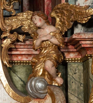 Zdjęcie nr 50: Ołtarz architektoniczny, trójosiowy, z wydzieloną częścią cokołową z bramkami bocznymi, jednokondygnacyjny, ze zwieńczeniem. Mensa drewniana z portatylem z marmuru dębnickiego, umieszczona na drewnianej, prostopadłościennej skrzyni.  Antepedium w kształcie leżącego prostokąta, ujęte profilowaną ramą dekorowaną liśćmi akantu i perełkowaniem. W polu płaskorzeźbione przedstawienie baranka leżącego na krzyżu, na obłoku, ujęte parą liści akantu oraz wicią roślinną z kwiatami i kiściami winogron. 
Na mensie tabernakulum z Tronem Łaski w formie prostopadłościanu na cokole, o wypukłej ściance frontowej, ujęte spływami wolutowymi podtrzymującymi niepełne belkowanie, wyłamane po środku łukiem półkolistym. Na froncie obrotowa nisza ujęta obramieniem w kształcie stojącego prostokąta zamkniętego łukiem nadwieszonym. W niszy ryte przedstawienie kielicha z Eucharystią w glorii, na obłoku, całość w rocaillowej ramie. Powyżej tron wystawienia z cokołem dekorowanym rocaille’em i parą ornamentalnych świeczników; ujęty parą kolumn dźwigających imposty. Podpory dżwigają rocaillowe kabłąki tworzące baldachim, na którego szczycie figurka baranka eucharystycznego leżącego na księdze. Ścianka w formie zbliżonej do stojącego prostokąta ujęta rocaille. Tabernakulum i tron ujęte okazałymi spływami wolutowymi z rocaillowymi uszami oraz na zakończeniach u dołu dwiema rzeźbami klęczących, adorujących aniołów.
Osie nastawy wydzielone w osiach skrajnych parą kolumn o skręconych trzonach i korynckich kapitelach umieszczonych na tle pilastrów, w osiach wewnętrznych parą pilastrów o trzonach w formie wolut z puttami z puttami, podtrzymywaną przez kariatydy w formie okazałych figur uskrzydlonych aniołów. Podpory wspierają pełne belkowanie z profilowanym gzymsem, występujące nad nimi, przerwane nad polem środkowym. W polu środkowym nisza ze sklepieniem kolebkowym wspartym na dwóch filarach i pilastrach. W głębi niszy obraz Św. Bartłomiej w profilowanej ramie w kształcie stojącego prostokąta zamkniętego łukiem odcinkowym. Na podniebiu niszy obraz Męczeństwo św. Bartłomieja w kształcie leżącego prostokąta ujętego niesymetrycznym obramieniem z motywem rocaille’ów. Nisza flankowana z figurami św. Stefana i św. Emeryka umieszczonymi na konsolach, na tle pilastrów. Pola retabulum w osiach skrajnych wklęsłe, między podporami prześwity z figurami św. Piotra i św. Pawła. W partii wysokiego cokołu bramki ujęte od zewnątrz wklęsłymi filarami podtrzymującymi belkowanie, wejścia z drzwiczkami w kształcie stojącego prostokąta zamkniętego łukiem półkolistym z obrazami przedstawiającymi Mojżesza i Aarona. Zwieńczenie w formie aedikuli ujętej pilastrami wspierającymi przerwane belkowanie oraz fantazyjnymi spływami wolutowymi, spływającymi na wewnętrzne podpory, przyjmując formę przerwanego przyczółka, na którym dwa putta i dwie figury siedzących aniołów. W osiach zewnętrznych podpór dwa putta siedzące kanelowanych postumentach i obłokach, prawe przytrzymuje skórę (atrybut św. Bartłomieja). W polu zwieńczenia obraz Św. Anna Samotrzeć w kształcie wydłużonego ośmioboku, w ornamentalnej ramie. Całość zwieńczona rzeźbioną półpostacią Boga Ojca pośród obłoków ukazanego w glorii promienistej. Drzwi do bramek flankowane liściastymi festonami, powyżej tarcze ujęte liśćmi laurowymi, zwieńczone koroną z klejnotem; lewa z klejnotem w postaci łabędzia z napisem: SOLI/ DEO/GLORIA, prawa z postacią ludzką z napisem: SOLI DEO HONOR. Woluty i fryz dekorowane motywami rocaille’ów oraz uskrzydlonymi główkami anielskimi. Osie boczne wypełnione ażurowymi rocaille’ami z gałązkami różanymi oraz ornamentem małżowinowo-chrząstkowym, belkowanie z podwieszonym lambrekinem z chwostami. Skręcone trzony kolumn zdobione wicią z winnej latorośli. Archiwolta nad polem środkowym dekorowana rocaille’em, rocaille’owym kartuszem i lambrekinem z chwostami. Woluty zwieńczenia, pilastry i naroża pola obrazowego dekorowane motywami rocaille’ów. 
Nastawa marmoryzowana w odcieniu jasnoszarym, profile marmoryzowane w kolorze jasnoróżowym, ornamenty i obramienia złocone.