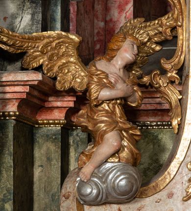 Zdjęcie nr 51: Ołtarz architektoniczny, trójosiowy, z wydzieloną częścią cokołową z bramkami bocznymi, jednokondygnacyjny, ze zwieńczeniem. Mensa drewniana z portatylem z marmuru dębnickiego, umieszczona na drewnianej, prostopadłościennej skrzyni.  Antepedium w kształcie leżącego prostokąta, ujęte profilowaną ramą dekorowaną liśćmi akantu i perełkowaniem. W polu płaskorzeźbione przedstawienie baranka leżącego na krzyżu, na obłoku, ujęte parą liści akantu oraz wicią roślinną z kwiatami i kiściami winogron. 
Na mensie tabernakulum z Tronem Łaski w formie prostopadłościanu na cokole, o wypukłej ściance frontowej, ujęte spływami wolutowymi podtrzymującymi niepełne belkowanie, wyłamane po środku łukiem półkolistym. Na froncie obrotowa nisza ujęta obramieniem w kształcie stojącego prostokąta zamkniętego łukiem nadwieszonym. W niszy ryte przedstawienie kielicha z Eucharystią w glorii, na obłoku, całość w rocaillowej ramie. Powyżej tron wystawienia z cokołem dekorowanym rocaille’em i parą ornamentalnych świeczników; ujęty parą kolumn dźwigających imposty. Podpory dżwigają rocaillowe kabłąki tworzące baldachim, na którego szczycie figurka baranka eucharystycznego leżącego na księdze. Ścianka w formie zbliżonej do stojącego prostokąta ujęta rocaille. Tabernakulum i tron ujęte okazałymi spływami wolutowymi z rocaillowymi uszami oraz na zakończeniach u dołu dwiema rzeźbami klęczących, adorujących aniołów.
Osie nastawy wydzielone w osiach skrajnych parą kolumn o skręconych trzonach i korynckich kapitelach umieszczonych na tle pilastrów, w osiach wewnętrznych parą pilastrów o trzonach w formie wolut z puttami z puttami, podtrzymywaną przez kariatydy w formie okazałych figur uskrzydlonych aniołów. Podpory wspierają pełne belkowanie z profilowanym gzymsem, występujące nad nimi, przerwane nad polem środkowym. W polu środkowym nisza ze sklepieniem kolebkowym wspartym na dwóch filarach i pilastrach. W głębi niszy obraz Św. Bartłomiej w profilowanej ramie w kształcie stojącego prostokąta zamkniętego łukiem odcinkowym. Na podniebiu niszy obraz Męczeństwo św. Bartłomieja w kształcie leżącego prostokąta ujętego niesymetrycznym obramieniem z motywem rocaille’ów. Nisza flankowana z figurami św. Stefana i św. Emeryka umieszczonymi na konsolach, na tle pilastrów. Pola retabulum w osiach skrajnych wklęsłe, między podporami prześwity z figurami św. Piotra i św. Pawła. W partii wysokiego cokołu bramki ujęte od zewnątrz wklęsłymi filarami podtrzymującymi belkowanie, wejścia z drzwiczkami w kształcie stojącego prostokąta zamkniętego łukiem półkolistym z obrazami przedstawiającymi Mojżesza i Aarona. Zwieńczenie w formie aedikuli ujętej pilastrami wspierającymi przerwane belkowanie oraz fantazyjnymi spływami wolutowymi, spływającymi na wewnętrzne podpory, przyjmując formę przerwanego przyczółka, na którym dwa putta i dwie figury siedzących aniołów. W osiach zewnętrznych podpór dwa putta siedzące kanelowanych postumentach i obłokach, prawe przytrzymuje skórę (atrybut św. Bartłomieja). W polu zwieńczenia obraz Św. Anna Samotrzeć w kształcie wydłużonego ośmioboku, w ornamentalnej ramie. Całość zwieńczona rzeźbioną półpostacią Boga Ojca pośród obłoków ukazanego w glorii promienistej. Drzwi do bramek flankowane liściastymi festonami, powyżej tarcze ujęte liśćmi laurowymi, zwieńczone koroną z klejnotem; lewa z klejnotem w postaci łabędzia z napisem: SOLI/ DEO/GLORIA, prawa z postacią ludzką z napisem: SOLI DEO HONOR. Woluty i fryz dekorowane motywami rocaille’ów oraz uskrzydlonymi główkami anielskimi. Osie boczne wypełnione ażurowymi rocaille’ami z gałązkami różanymi oraz ornamentem małżowinowo-chrząstkowym, belkowanie z podwieszonym lambrekinem z chwostami. Skręcone trzony kolumn zdobione wicią z winnej latorośli. Archiwolta nad polem środkowym dekorowana rocaille’em, rocaille’owym kartuszem i lambrekinem z chwostami. Woluty zwieńczenia, pilastry i naroża pola obrazowego dekorowane motywami rocaille’ów. 
Nastawa marmoryzowana w odcieniu jasnoszarym, profile marmoryzowane w kolorze jasnoróżowym, ornamenty i obramienia złocone.