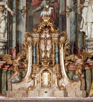 Zdjęcie nr 14: Ołtarz architektoniczny, trójosiowy, z wydzieloną częścią cokołową z bramkami bocznymi, jednokondygnacyjny, ze zwieńczeniem. Mensa drewniana z portatylem z marmuru dębnickiego, umieszczona na drewnianej, prostopadłościennej skrzyni.  Antepedium w kształcie leżącego prostokąta, ujęte profilowaną ramą dekorowaną liśćmi akantu i perełkowaniem. W polu płaskorzeźbione przedstawienie baranka leżącego na krzyżu, na obłoku, ujęte parą liści akantu oraz wicią roślinną z kwiatami i kiściami winogron. 
Na mensie tabernakulum z Tronem Łaski w formie prostopadłościanu na cokole, o wypukłej ściance frontowej, ujęte spływami wolutowymi podtrzymującymi niepełne belkowanie, wyłamane po środku łukiem półkolistym. Na froncie obrotowa nisza ujęta obramieniem w kształcie stojącego prostokąta zamkniętego łukiem nadwieszonym. W niszy ryte przedstawienie kielicha z Eucharystią w glorii, na obłoku, całość w rocaillowej ramie. Powyżej tron wystawienia z cokołem dekorowanym rocaille’em i parą ornamentalnych świeczników; ujęty parą kolumn dźwigających imposty. Podpory dżwigają rocaillowe kabłąki tworzące baldachim, na którego szczycie figurka baranka eucharystycznego leżącego na księdze. Ścianka w formie zbliżonej do stojącego prostokąta ujęta rocaille. Tabernakulum i tron ujęte okazałymi spływami wolutowymi z rocaillowymi uszami oraz na zakończeniach u dołu dwiema rzeźbami klęczących, adorujących aniołów.
Osie nastawy wydzielone w osiach skrajnych parą kolumn o skręconych trzonach i korynckich kapitelach umieszczonych na tle pilastrów, w osiach wewnętrznych parą pilastrów o trzonach w formie wolut z puttami z puttami, podtrzymywaną przez kariatydy w formie okazałych figur uskrzydlonych aniołów. Podpory wspierają pełne belkowanie z profilowanym gzymsem, występujące nad nimi, przerwane nad polem środkowym. W polu środkowym nisza ze sklepieniem kolebkowym wspartym na dwóch filarach i pilastrach. W głębi niszy obraz Św. Bartłomiej w profilowanej ramie w kształcie stojącego prostokąta zamkniętego łukiem odcinkowym. Na podniebiu niszy obraz Męczeństwo św. Bartłomieja w kształcie leżącego prostokąta ujętego niesymetrycznym obramieniem z motywem rocaille’ów. Nisza flankowana z figurami św. Stefana i św. Emeryka umieszczonymi na konsolach, na tle pilastrów. Pola retabulum w osiach skrajnych wklęsłe, między podporami prześwity z figurami św. Piotra i św. Pawła. W partii wysokiego cokołu bramki ujęte od zewnątrz wklęsłymi filarami podtrzymującymi belkowanie, wejścia z drzwiczkami w kształcie stojącego prostokąta zamkniętego łukiem półkolistym z obrazami przedstawiającymi Mojżesza i Aarona. Zwieńczenie w formie aedikuli ujętej pilastrami wspierającymi przerwane belkowanie oraz fantazyjnymi spływami wolutowymi, spływającymi na wewnętrzne podpory, przyjmując formę przerwanego przyczółka, na którym dwa putta i dwie figury siedzących aniołów. W osiach zewnętrznych podpór dwa putta siedzące kanelowanych postumentach i obłokach, prawe przytrzymuje skórę (atrybut św. Bartłomieja). W polu zwieńczenia obraz Św. Anna Samotrzeć w kształcie wydłużonego ośmioboku, w ornamentalnej ramie. Całość zwieńczona rzeźbioną półpostacią Boga Ojca pośród obłoków ukazanego w glorii promienistej. Drzwi do bramek flankowane liściastymi festonami, powyżej tarcze ujęte liśćmi laurowymi, zwieńczone koroną z klejnotem; lewa z klejnotem w postaci łabędzia z napisem: SOLI/ DEO/GLORIA, prawa z postacią ludzką z napisem: SOLI DEO HONOR. Woluty i fryz dekorowane motywami rocaille’ów oraz uskrzydlonymi główkami anielskimi. Osie boczne wypełnione ażurowymi rocaille’ami z gałązkami różanymi oraz ornamentem małżowinowo-chrząstkowym, belkowanie z podwieszonym lambrekinem z chwostami. Skręcone trzony kolumn zdobione wicią z winnej latorośli. Archiwolta nad polem środkowym dekorowana rocaille’em, rocaille’owym kartuszem i lambrekinem z chwostami. Woluty zwieńczenia, pilastry i naroża pola obrazowego dekorowane motywami rocaille’ów. 
Nastawa marmoryzowana w odcieniu jasnoszarym, profile marmoryzowane w kolorze jasnoróżowym, ornamenty i obramienia złocone.