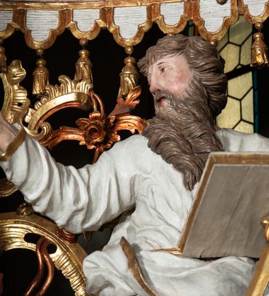 Zdjęcie nr 20: Ołtarz architektoniczny, trójosiowy, z wydzieloną częścią cokołową z bramkami bocznymi, jednokondygnacyjny, ze zwieńczeniem. Mensa drewniana z portatylem z marmuru dębnickiego, umieszczona na drewnianej, prostopadłościennej skrzyni.  Antepedium w kształcie leżącego prostokąta, ujęte profilowaną ramą dekorowaną liśćmi akantu i perełkowaniem. W polu płaskorzeźbione przedstawienie baranka leżącego na krzyżu, na obłoku, ujęte parą liści akantu oraz wicią roślinną z kwiatami i kiściami winogron. 
Na mensie tabernakulum z Tronem Łaski w formie prostopadłościanu na cokole, o wypukłej ściance frontowej, ujęte spływami wolutowymi podtrzymującymi niepełne belkowanie, wyłamane po środku łukiem półkolistym. Na froncie obrotowa nisza ujęta obramieniem w kształcie stojącego prostokąta zamkniętego łukiem nadwieszonym. W niszy ryte przedstawienie kielicha z Eucharystią w glorii, na obłoku, całość w rocaillowej ramie. Powyżej tron wystawienia z cokołem dekorowanym rocaille’em i parą ornamentalnych świeczników; ujęty parą kolumn dźwigających imposty. Podpory dżwigają rocaillowe kabłąki tworzące baldachim, na którego szczycie figurka baranka eucharystycznego leżącego na księdze. Ścianka w formie zbliżonej do stojącego prostokąta ujęta rocaille. Tabernakulum i tron ujęte okazałymi spływami wolutowymi z rocaillowymi uszami oraz na zakończeniach u dołu dwiema rzeźbami klęczących, adorujących aniołów.
Osie nastawy wydzielone w osiach skrajnych parą kolumn o skręconych trzonach i korynckich kapitelach umieszczonych na tle pilastrów, w osiach wewnętrznych parą pilastrów o trzonach w formie wolut z puttami z puttami, podtrzymywaną przez kariatydy w formie okazałych figur uskrzydlonych aniołów. Podpory wspierają pełne belkowanie z profilowanym gzymsem, występujące nad nimi, przerwane nad polem środkowym. W polu środkowym nisza ze sklepieniem kolebkowym wspartym na dwóch filarach i pilastrach. W głębi niszy obraz Św. Bartłomiej w profilowanej ramie w kształcie stojącego prostokąta zamkniętego łukiem odcinkowym. Na podniebiu niszy obraz Męczeństwo św. Bartłomieja w kształcie leżącego prostokąta ujętego niesymetrycznym obramieniem z motywem rocaille’ów. Nisza flankowana z figurami św. Stefana i św. Emeryka umieszczonymi na konsolach, na tle pilastrów. Pola retabulum w osiach skrajnych wklęsłe, między podporami prześwity z figurami św. Piotra i św. Pawła. W partii wysokiego cokołu bramki ujęte od zewnątrz wklęsłymi filarami podtrzymującymi belkowanie, wejścia z drzwiczkami w kształcie stojącego prostokąta zamkniętego łukiem półkolistym z obrazami przedstawiającymi Mojżesza i Aarona. Zwieńczenie w formie aedikuli ujętej pilastrami wspierającymi przerwane belkowanie oraz fantazyjnymi spływami wolutowymi, spływającymi na wewnętrzne podpory, przyjmując formę przerwanego przyczółka, na którym dwa putta i dwie figury siedzących aniołów. W osiach zewnętrznych podpór dwa putta siedzące kanelowanych postumentach i obłokach, prawe przytrzymuje skórę (atrybut św. Bartłomieja). W polu zwieńczenia obraz Św. Anna Samotrzeć w kształcie wydłużonego ośmioboku, w ornamentalnej ramie. Całość zwieńczona rzeźbioną półpostacią Boga Ojca pośród obłoków ukazanego w glorii promienistej. Drzwi do bramek flankowane liściastymi festonami, powyżej tarcze ujęte liśćmi laurowymi, zwieńczone koroną z klejnotem; lewa z klejnotem w postaci łabędzia z napisem: SOLI/ DEO/GLORIA, prawa z postacią ludzką z napisem: SOLI DEO HONOR. Woluty i fryz dekorowane motywami rocaille’ów oraz uskrzydlonymi główkami anielskimi. Osie boczne wypełnione ażurowymi rocaille’ami z gałązkami różanymi oraz ornamentem małżowinowo-chrząstkowym, belkowanie z podwieszonym lambrekinem z chwostami. Skręcone trzony kolumn zdobione wicią z winnej latorośli. Archiwolta nad polem środkowym dekorowana rocaille’em, rocaille’owym kartuszem i lambrekinem z chwostami. Woluty zwieńczenia, pilastry i naroża pola obrazowego dekorowane motywami rocaille’ów. 
Nastawa marmoryzowana w odcieniu jasnoszarym, profile marmoryzowane w kolorze jasnoróżowym, ornamenty i obramienia złocone.