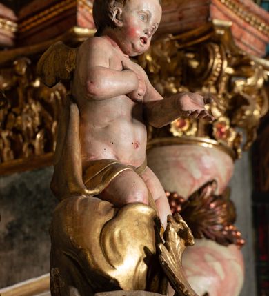 Zdjęcie nr 57: Ołtarz architektoniczny, trójosiowy, z wydzieloną częścią cokołową z bramkami bocznymi, jednokondygnacyjny, ze zwieńczeniem. Mensa drewniana z portatylem z marmuru dębnickiego, umieszczona na drewnianej, prostopadłościennej skrzyni.  Antepedium w kształcie leżącego prostokąta, ujęte profilowaną ramą dekorowaną liśćmi akantu i perełkowaniem. W polu płaskorzeźbione przedstawienie baranka leżącego na krzyżu, na obłoku, ujęte parą liści akantu oraz wicią roślinną z kwiatami i kiściami winogron. 
Na mensie tabernakulum z Tronem Łaski w formie prostopadłościanu na cokole, o wypukłej ściance frontowej, ujęte spływami wolutowymi podtrzymującymi niepełne belkowanie, wyłamane po środku łukiem półkolistym. Na froncie obrotowa nisza ujęta obramieniem w kształcie stojącego prostokąta zamkniętego łukiem nadwieszonym. W niszy ryte przedstawienie kielicha z Eucharystią w glorii, na obłoku, całość w rocaillowej ramie. Powyżej tron wystawienia z cokołem dekorowanym rocaille’em i parą ornamentalnych świeczników; ujęty parą kolumn dźwigających imposty. Podpory dżwigają rocaillowe kabłąki tworzące baldachim, na którego szczycie figurka baranka eucharystycznego leżącego na księdze. Ścianka w formie zbliżonej do stojącego prostokąta ujęta rocaille. Tabernakulum i tron ujęte okazałymi spływami wolutowymi z rocaillowymi uszami oraz na zakończeniach u dołu dwiema rzeźbami klęczących, adorujących aniołów.
Osie nastawy wydzielone w osiach skrajnych parą kolumn o skręconych trzonach i korynckich kapitelach umieszczonych na tle pilastrów, w osiach wewnętrznych parą pilastrów o trzonach w formie wolut z puttami z puttami, podtrzymywaną przez kariatydy w formie okazałych figur uskrzydlonych aniołów. Podpory wspierają pełne belkowanie z profilowanym gzymsem, występujące nad nimi, przerwane nad polem środkowym. W polu środkowym nisza ze sklepieniem kolebkowym wspartym na dwóch filarach i pilastrach. W głębi niszy obraz Św. Bartłomiej w profilowanej ramie w kształcie stojącego prostokąta zamkniętego łukiem odcinkowym. Na podniebiu niszy obraz Męczeństwo św. Bartłomieja w kształcie leżącego prostokąta ujętego niesymetrycznym obramieniem z motywem rocaille’ów. Nisza flankowana z figurami św. Stefana i św. Emeryka umieszczonymi na konsolach, na tle pilastrów. Pola retabulum w osiach skrajnych wklęsłe, między podporami prześwity z figurami św. Piotra i św. Pawła. W partii wysokiego cokołu bramki ujęte od zewnątrz wklęsłymi filarami podtrzymującymi belkowanie, wejścia z drzwiczkami w kształcie stojącego prostokąta zamkniętego łukiem półkolistym z obrazami przedstawiającymi Mojżesza i Aarona. Zwieńczenie w formie aedikuli ujętej pilastrami wspierającymi przerwane belkowanie oraz fantazyjnymi spływami wolutowymi, spływającymi na wewnętrzne podpory, przyjmując formę przerwanego przyczółka, na którym dwa putta i dwie figury siedzących aniołów. W osiach zewnętrznych podpór dwa putta siedzące kanelowanych postumentach i obłokach, prawe przytrzymuje skórę (atrybut św. Bartłomieja). W polu zwieńczenia obraz Św. Anna Samotrzeć w kształcie wydłużonego ośmioboku, w ornamentalnej ramie. Całość zwieńczona rzeźbioną półpostacią Boga Ojca pośród obłoków ukazanego w glorii promienistej. Drzwi do bramek flankowane liściastymi festonami, powyżej tarcze ujęte liśćmi laurowymi, zwieńczone koroną z klejnotem; lewa z klejnotem w postaci łabędzia z napisem: SOLI/ DEO/GLORIA, prawa z postacią ludzką z napisem: SOLI DEO HONOR. Woluty i fryz dekorowane motywami rocaille’ów oraz uskrzydlonymi główkami anielskimi. Osie boczne wypełnione ażurowymi rocaille’ami z gałązkami różanymi oraz ornamentem małżowinowo-chrząstkowym, belkowanie z podwieszonym lambrekinem z chwostami. Skręcone trzony kolumn zdobione wicią z winnej latorośli. Archiwolta nad polem środkowym dekorowana rocaille’em, rocaille’owym kartuszem i lambrekinem z chwostami. Woluty zwieńczenia, pilastry i naroża pola obrazowego dekorowane motywami rocaille’ów. 
Nastawa marmoryzowana w odcieniu jasnoszarym, profile marmoryzowane w kolorze jasnoróżowym, ornamenty i obramienia złocone.