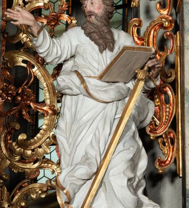 Zdjęcie nr 22: Ołtarz architektoniczny, trójosiowy, z wydzieloną częścią cokołową z bramkami bocznymi, jednokondygnacyjny, ze zwieńczeniem. Mensa drewniana z portatylem z marmuru dębnickiego, umieszczona na drewnianej, prostopadłościennej skrzyni.  Antepedium w kształcie leżącego prostokąta, ujęte profilowaną ramą dekorowaną liśćmi akantu i perełkowaniem. W polu płaskorzeźbione przedstawienie baranka leżącego na krzyżu, na obłoku, ujęte parą liści akantu oraz wicią roślinną z kwiatami i kiściami winogron. 
Na mensie tabernakulum z Tronem Łaski w formie prostopadłościanu na cokole, o wypukłej ściance frontowej, ujęte spływami wolutowymi podtrzymującymi niepełne belkowanie, wyłamane po środku łukiem półkolistym. Na froncie obrotowa nisza ujęta obramieniem w kształcie stojącego prostokąta zamkniętego łukiem nadwieszonym. W niszy ryte przedstawienie kielicha z Eucharystią w glorii, na obłoku, całość w rocaillowej ramie. Powyżej tron wystawienia z cokołem dekorowanym rocaille’em i parą ornamentalnych świeczników; ujęty parą kolumn dźwigających imposty. Podpory dżwigają rocaillowe kabłąki tworzące baldachim, na którego szczycie figurka baranka eucharystycznego leżącego na księdze. Ścianka w formie zbliżonej do stojącego prostokąta ujęta rocaille. Tabernakulum i tron ujęte okazałymi spływami wolutowymi z rocaillowymi uszami oraz na zakończeniach u dołu dwiema rzeźbami klęczących, adorujących aniołów.
Osie nastawy wydzielone w osiach skrajnych parą kolumn o skręconych trzonach i korynckich kapitelach umieszczonych na tle pilastrów, w osiach wewnętrznych parą pilastrów o trzonach w formie wolut z puttami z puttami, podtrzymywaną przez kariatydy w formie okazałych figur uskrzydlonych aniołów. Podpory wspierają pełne belkowanie z profilowanym gzymsem, występujące nad nimi, przerwane nad polem środkowym. W polu środkowym nisza ze sklepieniem kolebkowym wspartym na dwóch filarach i pilastrach. W głębi niszy obraz Św. Bartłomiej w profilowanej ramie w kształcie stojącego prostokąta zamkniętego łukiem odcinkowym. Na podniebiu niszy obraz Męczeństwo św. Bartłomieja w kształcie leżącego prostokąta ujętego niesymetrycznym obramieniem z motywem rocaille’ów. Nisza flankowana z figurami św. Stefana i św. Emeryka umieszczonymi na konsolach, na tle pilastrów. Pola retabulum w osiach skrajnych wklęsłe, między podporami prześwity z figurami św. Piotra i św. Pawła. W partii wysokiego cokołu bramki ujęte od zewnątrz wklęsłymi filarami podtrzymującymi belkowanie, wejścia z drzwiczkami w kształcie stojącego prostokąta zamkniętego łukiem półkolistym z obrazami przedstawiającymi Mojżesza i Aarona. Zwieńczenie w formie aedikuli ujętej pilastrami wspierającymi przerwane belkowanie oraz fantazyjnymi spływami wolutowymi, spływającymi na wewnętrzne podpory, przyjmując formę przerwanego przyczółka, na którym dwa putta i dwie figury siedzących aniołów. W osiach zewnętrznych podpór dwa putta siedzące kanelowanych postumentach i obłokach, prawe przytrzymuje skórę (atrybut św. Bartłomieja). W polu zwieńczenia obraz Św. Anna Samotrzeć w kształcie wydłużonego ośmioboku, w ornamentalnej ramie. Całość zwieńczona rzeźbioną półpostacią Boga Ojca pośród obłoków ukazanego w glorii promienistej. Drzwi do bramek flankowane liściastymi festonami, powyżej tarcze ujęte liśćmi laurowymi, zwieńczone koroną z klejnotem; lewa z klejnotem w postaci łabędzia z napisem: SOLI/ DEO/GLORIA, prawa z postacią ludzką z napisem: SOLI DEO HONOR. Woluty i fryz dekorowane motywami rocaille’ów oraz uskrzydlonymi główkami anielskimi. Osie boczne wypełnione ażurowymi rocaille’ami z gałązkami różanymi oraz ornamentem małżowinowo-chrząstkowym, belkowanie z podwieszonym lambrekinem z chwostami. Skręcone trzony kolumn zdobione wicią z winnej latorośli. Archiwolta nad polem środkowym dekorowana rocaille’em, rocaille’owym kartuszem i lambrekinem z chwostami. Woluty zwieńczenia, pilastry i naroża pola obrazowego dekorowane motywami rocaille’ów. 
Nastawa marmoryzowana w odcieniu jasnoszarym, profile marmoryzowane w kolorze jasnoróżowym, ornamenty i obramienia złocone.