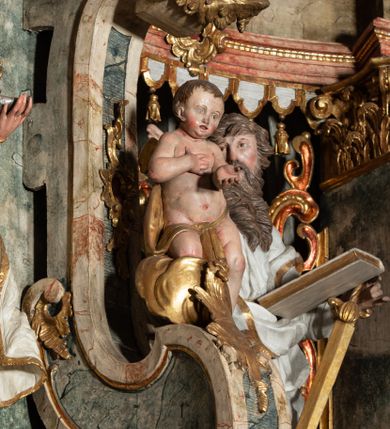 Zdjęcie nr 53: Ołtarz architektoniczny, trójosiowy, z wydzieloną częścią cokołową z bramkami bocznymi, jednokondygnacyjny, ze zwieńczeniem. Mensa drewniana z portatylem z marmuru dębnickiego, umieszczona na drewnianej, prostopadłościennej skrzyni.  Antepedium w kształcie leżącego prostokąta, ujęte profilowaną ramą dekorowaną liśćmi akantu i perełkowaniem. W polu płaskorzeźbione przedstawienie baranka leżącego na krzyżu, na obłoku, ujęte parą liści akantu oraz wicią roślinną z kwiatami i kiściami winogron. 
Na mensie tabernakulum z Tronem Łaski w formie prostopadłościanu na cokole, o wypukłej ściance frontowej, ujęte spływami wolutowymi podtrzymującymi niepełne belkowanie, wyłamane po środku łukiem półkolistym. Na froncie obrotowa nisza ujęta obramieniem w kształcie stojącego prostokąta zamkniętego łukiem nadwieszonym. W niszy ryte przedstawienie kielicha z Eucharystią w glorii, na obłoku, całość w rocaillowej ramie. Powyżej tron wystawienia z cokołem dekorowanym rocaille’em i parą ornamentalnych świeczników; ujęty parą kolumn dźwigających imposty. Podpory dżwigają rocaillowe kabłąki tworzące baldachim, na którego szczycie figurka baranka eucharystycznego leżącego na księdze. Ścianka w formie zbliżonej do stojącego prostokąta ujęta rocaille. Tabernakulum i tron ujęte okazałymi spływami wolutowymi z rocaillowymi uszami oraz na zakończeniach u dołu dwiema rzeźbami klęczących, adorujących aniołów.
Osie nastawy wydzielone w osiach skrajnych parą kolumn o skręconych trzonach i korynckich kapitelach umieszczonych na tle pilastrów, w osiach wewnętrznych parą pilastrów o trzonach w formie wolut z puttami z puttami, podtrzymywaną przez kariatydy w formie okazałych figur uskrzydlonych aniołów. Podpory wspierają pełne belkowanie z profilowanym gzymsem, występujące nad nimi, przerwane nad polem środkowym. W polu środkowym nisza ze sklepieniem kolebkowym wspartym na dwóch filarach i pilastrach. W głębi niszy obraz Św. Bartłomiej w profilowanej ramie w kształcie stojącego prostokąta zamkniętego łukiem odcinkowym. Na podniebiu niszy obraz Męczeństwo św. Bartłomieja w kształcie leżącego prostokąta ujętego niesymetrycznym obramieniem z motywem rocaille’ów. Nisza flankowana z figurami św. Stefana i św. Emeryka umieszczonymi na konsolach, na tle pilastrów. Pola retabulum w osiach skrajnych wklęsłe, między podporami prześwity z figurami św. Piotra i św. Pawła. W partii wysokiego cokołu bramki ujęte od zewnątrz wklęsłymi filarami podtrzymującymi belkowanie, wejścia z drzwiczkami w kształcie stojącego prostokąta zamkniętego łukiem półkolistym z obrazami przedstawiającymi Mojżesza i Aarona. Zwieńczenie w formie aedikuli ujętej pilastrami wspierającymi przerwane belkowanie oraz fantazyjnymi spływami wolutowymi, spływającymi na wewnętrzne podpory, przyjmując formę przerwanego przyczółka, na którym dwa putta i dwie figury siedzących aniołów. W osiach zewnętrznych podpór dwa putta siedzące kanelowanych postumentach i obłokach, prawe przytrzymuje skórę (atrybut św. Bartłomieja). W polu zwieńczenia obraz Św. Anna Samotrzeć w kształcie wydłużonego ośmioboku, w ornamentalnej ramie. Całość zwieńczona rzeźbioną półpostacią Boga Ojca pośród obłoków ukazanego w glorii promienistej. Drzwi do bramek flankowane liściastymi festonami, powyżej tarcze ujęte liśćmi laurowymi, zwieńczone koroną z klejnotem; lewa z klejnotem w postaci łabędzia z napisem: SOLI/ DEO/GLORIA, prawa z postacią ludzką z napisem: SOLI DEO HONOR. Woluty i fryz dekorowane motywami rocaille’ów oraz uskrzydlonymi główkami anielskimi. Osie boczne wypełnione ażurowymi rocaille’ami z gałązkami różanymi oraz ornamentem małżowinowo-chrząstkowym, belkowanie z podwieszonym lambrekinem z chwostami. Skręcone trzony kolumn zdobione wicią z winnej latorośli. Archiwolta nad polem środkowym dekorowana rocaille’em, rocaille’owym kartuszem i lambrekinem z chwostami. Woluty zwieńczenia, pilastry i naroża pola obrazowego dekorowane motywami rocaille’ów. 
Nastawa marmoryzowana w odcieniu jasnoszarym, profile marmoryzowane w kolorze jasnoróżowym, ornamenty i obramienia złocone.