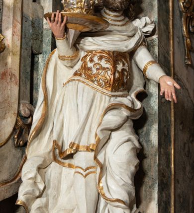 Zdjęcie nr 31: Ołtarz architektoniczny, trójosiowy, z wydzieloną częścią cokołową z bramkami bocznymi, jednokondygnacyjny, ze zwieńczeniem. Mensa drewniana z portatylem z marmuru dębnickiego, umieszczona na drewnianej, prostopadłościennej skrzyni.  Antepedium w kształcie leżącego prostokąta, ujęte profilowaną ramą dekorowaną liśćmi akantu i perełkowaniem. W polu płaskorzeźbione przedstawienie baranka leżącego na krzyżu, na obłoku, ujęte parą liści akantu oraz wicią roślinną z kwiatami i kiściami winogron. 
Na mensie tabernakulum z Tronem Łaski w formie prostopadłościanu na cokole, o wypukłej ściance frontowej, ujęte spływami wolutowymi podtrzymującymi niepełne belkowanie, wyłamane po środku łukiem półkolistym. Na froncie obrotowa nisza ujęta obramieniem w kształcie stojącego prostokąta zamkniętego łukiem nadwieszonym. W niszy ryte przedstawienie kielicha z Eucharystią w glorii, na obłoku, całość w rocaillowej ramie. Powyżej tron wystawienia z cokołem dekorowanym rocaille’em i parą ornamentalnych świeczników; ujęty parą kolumn dźwigających imposty. Podpory dżwigają rocaillowe kabłąki tworzące baldachim, na którego szczycie figurka baranka eucharystycznego leżącego na księdze. Ścianka w formie zbliżonej do stojącego prostokąta ujęta rocaille. Tabernakulum i tron ujęte okazałymi spływami wolutowymi z rocaillowymi uszami oraz na zakończeniach u dołu dwiema rzeźbami klęczących, adorujących aniołów.
Osie nastawy wydzielone w osiach skrajnych parą kolumn o skręconych trzonach i korynckich kapitelach umieszczonych na tle pilastrów, w osiach wewnętrznych parą pilastrów o trzonach w formie wolut z puttami z puttami, podtrzymywaną przez kariatydy w formie okazałych figur uskrzydlonych aniołów. Podpory wspierają pełne belkowanie z profilowanym gzymsem, występujące nad nimi, przerwane nad polem środkowym. W polu środkowym nisza ze sklepieniem kolebkowym wspartym na dwóch filarach i pilastrach. W głębi niszy obraz Św. Bartłomiej w profilowanej ramie w kształcie stojącego prostokąta zamkniętego łukiem odcinkowym. Na podniebiu niszy obraz Męczeństwo św. Bartłomieja w kształcie leżącego prostokąta ujętego niesymetrycznym obramieniem z motywem rocaille’ów. Nisza flankowana z figurami św. Stefana i św. Emeryka umieszczonymi na konsolach, na tle pilastrów. Pola retabulum w osiach skrajnych wklęsłe, między podporami prześwity z figurami św. Piotra i św. Pawła. W partii wysokiego cokołu bramki ujęte od zewnątrz wklęsłymi filarami podtrzymującymi belkowanie, wejścia z drzwiczkami w kształcie stojącego prostokąta zamkniętego łukiem półkolistym z obrazami przedstawiającymi Mojżesza i Aarona. Zwieńczenie w formie aedikuli ujętej pilastrami wspierającymi przerwane belkowanie oraz fantazyjnymi spływami wolutowymi, spływającymi na wewnętrzne podpory, przyjmując formę przerwanego przyczółka, na którym dwa putta i dwie figury siedzących aniołów. W osiach zewnętrznych podpór dwa putta siedzące kanelowanych postumentach i obłokach, prawe przytrzymuje skórę (atrybut św. Bartłomieja). W polu zwieńczenia obraz Św. Anna Samotrzeć w kształcie wydłużonego ośmioboku, w ornamentalnej ramie. Całość zwieńczona rzeźbioną półpostacią Boga Ojca pośród obłoków ukazanego w glorii promienistej. Drzwi do bramek flankowane liściastymi festonami, powyżej tarcze ujęte liśćmi laurowymi, zwieńczone koroną z klejnotem; lewa z klejnotem w postaci łabędzia z napisem: SOLI/ DEO/GLORIA, prawa z postacią ludzką z napisem: SOLI DEO HONOR. Woluty i fryz dekorowane motywami rocaille’ów oraz uskrzydlonymi główkami anielskimi. Osie boczne wypełnione ażurowymi rocaille’ami z gałązkami różanymi oraz ornamentem małżowinowo-chrząstkowym, belkowanie z podwieszonym lambrekinem z chwostami. Skręcone trzony kolumn zdobione wicią z winnej latorośli. Archiwolta nad polem środkowym dekorowana rocaille’em, rocaille’owym kartuszem i lambrekinem z chwostami. Woluty zwieńczenia, pilastry i naroża pola obrazowego dekorowane motywami rocaille’ów. 
Nastawa marmoryzowana w odcieniu jasnoszarym, profile marmoryzowane w kolorze jasnoróżowym, ornamenty i obramienia złocone.