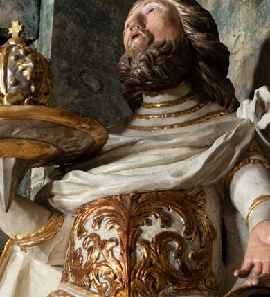 Zdjęcie nr 29: Ołtarz architektoniczny, trójosiowy, z wydzieloną częścią cokołową z bramkami bocznymi, jednokondygnacyjny, ze zwieńczeniem. Mensa drewniana z portatylem z marmuru dębnickiego, umieszczona na drewnianej, prostopadłościennej skrzyni.  Antepedium w kształcie leżącego prostokąta, ujęte profilowaną ramą dekorowaną liśćmi akantu i perełkowaniem. W polu płaskorzeźbione przedstawienie baranka leżącego na krzyżu, na obłoku, ujęte parą liści akantu oraz wicią roślinną z kwiatami i kiściami winogron. 
Na mensie tabernakulum z Tronem Łaski w formie prostopadłościanu na cokole, o wypukłej ściance frontowej, ujęte spływami wolutowymi podtrzymującymi niepełne belkowanie, wyłamane po środku łukiem półkolistym. Na froncie obrotowa nisza ujęta obramieniem w kształcie stojącego prostokąta zamkniętego łukiem nadwieszonym. W niszy ryte przedstawienie kielicha z Eucharystią w glorii, na obłoku, całość w rocaillowej ramie. Powyżej tron wystawienia z cokołem dekorowanym rocaille’em i parą ornamentalnych świeczników; ujęty parą kolumn dźwigających imposty. Podpory dżwigają rocaillowe kabłąki tworzące baldachim, na którego szczycie figurka baranka eucharystycznego leżącego na księdze. Ścianka w formie zbliżonej do stojącego prostokąta ujęta rocaille. Tabernakulum i tron ujęte okazałymi spływami wolutowymi z rocaillowymi uszami oraz na zakończeniach u dołu dwiema rzeźbami klęczących, adorujących aniołów.
Osie nastawy wydzielone w osiach skrajnych parą kolumn o skręconych trzonach i korynckich kapitelach umieszczonych na tle pilastrów, w osiach wewnętrznych parą pilastrów o trzonach w formie wolut z puttami z puttami, podtrzymywaną przez kariatydy w formie okazałych figur uskrzydlonych aniołów. Podpory wspierają pełne belkowanie z profilowanym gzymsem, występujące nad nimi, przerwane nad polem środkowym. W polu środkowym nisza ze sklepieniem kolebkowym wspartym na dwóch filarach i pilastrach. W głębi niszy obraz Św. Bartłomiej w profilowanej ramie w kształcie stojącego prostokąta zamkniętego łukiem odcinkowym. Na podniebiu niszy obraz Męczeństwo św. Bartłomieja w kształcie leżącego prostokąta ujętego niesymetrycznym obramieniem z motywem rocaille’ów. Nisza flankowana z figurami św. Stefana i św. Emeryka umieszczonymi na konsolach, na tle pilastrów. Pola retabulum w osiach skrajnych wklęsłe, między podporami prześwity z figurami św. Piotra i św. Pawła. W partii wysokiego cokołu bramki ujęte od zewnątrz wklęsłymi filarami podtrzymującymi belkowanie, wejścia z drzwiczkami w kształcie stojącego prostokąta zamkniętego łukiem półkolistym z obrazami przedstawiającymi Mojżesza i Aarona. Zwieńczenie w formie aedikuli ujętej pilastrami wspierającymi przerwane belkowanie oraz fantazyjnymi spływami wolutowymi, spływającymi na wewnętrzne podpory, przyjmując formę przerwanego przyczółka, na którym dwa putta i dwie figury siedzących aniołów. W osiach zewnętrznych podpór dwa putta siedzące kanelowanych postumentach i obłokach, prawe przytrzymuje skórę (atrybut św. Bartłomieja). W polu zwieńczenia obraz Św. Anna Samotrzeć w kształcie wydłużonego ośmioboku, w ornamentalnej ramie. Całość zwieńczona rzeźbioną półpostacią Boga Ojca pośród obłoków ukazanego w glorii promienistej. Drzwi do bramek flankowane liściastymi festonami, powyżej tarcze ujęte liśćmi laurowymi, zwieńczone koroną z klejnotem; lewa z klejnotem w postaci łabędzia z napisem: SOLI/ DEO/GLORIA, prawa z postacią ludzką z napisem: SOLI DEO HONOR. Woluty i fryz dekorowane motywami rocaille’ów oraz uskrzydlonymi główkami anielskimi. Osie boczne wypełnione ażurowymi rocaille’ami z gałązkami różanymi oraz ornamentem małżowinowo-chrząstkowym, belkowanie z podwieszonym lambrekinem z chwostami. Skręcone trzony kolumn zdobione wicią z winnej latorośli. Archiwolta nad polem środkowym dekorowana rocaille’em, rocaille’owym kartuszem i lambrekinem z chwostami. Woluty zwieńczenia, pilastry i naroża pola obrazowego dekorowane motywami rocaille’ów. 
Nastawa marmoryzowana w odcieniu jasnoszarym, profile marmoryzowane w kolorze jasnoróżowym, ornamenty i obramienia złocone.