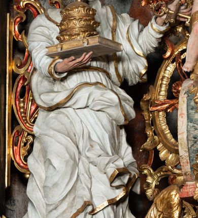 Zdjęcie nr 34: Ołtarz architektoniczny, trójosiowy, z wydzieloną częścią cokołową z bramkami bocznymi, jednokondygnacyjny, ze zwieńczeniem. Mensa drewniana z portatylem z marmuru dębnickiego, umieszczona na drewnianej, prostopadłościennej skrzyni.  Antepedium w kształcie leżącego prostokąta, ujęte profilowaną ramą dekorowaną liśćmi akantu i perełkowaniem. W polu płaskorzeźbione przedstawienie baranka leżącego na krzyżu, na obłoku, ujęte parą liści akantu oraz wicią roślinną z kwiatami i kiściami winogron. 
Na mensie tabernakulum z Tronem Łaski w formie prostopadłościanu na cokole, o wypukłej ściance frontowej, ujęte spływami wolutowymi podtrzymującymi niepełne belkowanie, wyłamane po środku łukiem półkolistym. Na froncie obrotowa nisza ujęta obramieniem w kształcie stojącego prostokąta zamkniętego łukiem nadwieszonym. W niszy ryte przedstawienie kielicha z Eucharystią w glorii, na obłoku, całość w rocaillowej ramie. Powyżej tron wystawienia z cokołem dekorowanym rocaille’em i parą ornamentalnych świeczników; ujęty parą kolumn dźwigających imposty. Podpory dżwigają rocaillowe kabłąki tworzące baldachim, na którego szczycie figurka baranka eucharystycznego leżącego na księdze. Ścianka w formie zbliżonej do stojącego prostokąta ujęta rocaille. Tabernakulum i tron ujęte okazałymi spływami wolutowymi z rocaillowymi uszami oraz na zakończeniach u dołu dwiema rzeźbami klęczących, adorujących aniołów.
Osie nastawy wydzielone w osiach skrajnych parą kolumn o skręconych trzonach i korynckich kapitelach umieszczonych na tle pilastrów, w osiach wewnętrznych parą pilastrów o trzonach w formie wolut z puttami z puttami, podtrzymywaną przez kariatydy w formie okazałych figur uskrzydlonych aniołów. Podpory wspierają pełne belkowanie z profilowanym gzymsem, występujące nad nimi, przerwane nad polem środkowym. W polu środkowym nisza ze sklepieniem kolebkowym wspartym na dwóch filarach i pilastrach. W głębi niszy obraz Św. Bartłomiej w profilowanej ramie w kształcie stojącego prostokąta zamkniętego łukiem odcinkowym. Na podniebiu niszy obraz Męczeństwo św. Bartłomieja w kształcie leżącego prostokąta ujętego niesymetrycznym obramieniem z motywem rocaille’ów. Nisza flankowana z figurami św. Stefana i św. Emeryka umieszczonymi na konsolach, na tle pilastrów. Pola retabulum w osiach skrajnych wklęsłe, między podporami prześwity z figurami św. Piotra i św. Pawła. W partii wysokiego cokołu bramki ujęte od zewnątrz wklęsłymi filarami podtrzymującymi belkowanie, wejścia z drzwiczkami w kształcie stojącego prostokąta zamkniętego łukiem półkolistym z obrazami przedstawiającymi Mojżesza i Aarona. Zwieńczenie w formie aedikuli ujętej pilastrami wspierającymi przerwane belkowanie oraz fantazyjnymi spływami wolutowymi, spływającymi na wewnętrzne podpory, przyjmując formę przerwanego przyczółka, na którym dwa putta i dwie figury siedzących aniołów. W osiach zewnętrznych podpór dwa putta siedzące kanelowanych postumentach i obłokach, prawe przytrzymuje skórę (atrybut św. Bartłomieja). W polu zwieńczenia obraz Św. Anna Samotrzeć w kształcie wydłużonego ośmioboku, w ornamentalnej ramie. Całość zwieńczona rzeźbioną półpostacią Boga Ojca pośród obłoków ukazanego w glorii promienistej. Drzwi do bramek flankowane liściastymi festonami, powyżej tarcze ujęte liśćmi laurowymi, zwieńczone koroną z klejnotem; lewa z klejnotem w postaci łabędzia z napisem: SOLI/ DEO/GLORIA, prawa z postacią ludzką z napisem: SOLI DEO HONOR. Woluty i fryz dekorowane motywami rocaille’ów oraz uskrzydlonymi główkami anielskimi. Osie boczne wypełnione ażurowymi rocaille’ami z gałązkami różanymi oraz ornamentem małżowinowo-chrząstkowym, belkowanie z podwieszonym lambrekinem z chwostami. Skręcone trzony kolumn zdobione wicią z winnej latorośli. Archiwolta nad polem środkowym dekorowana rocaille’em, rocaille’owym kartuszem i lambrekinem z chwostami. Woluty zwieńczenia, pilastry i naroża pola obrazowego dekorowane motywami rocaille’ów. 
Nastawa marmoryzowana w odcieniu jasnoszarym, profile marmoryzowane w kolorze jasnoróżowym, ornamenty i obramienia złocone.