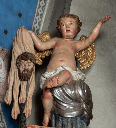 Zdjęcie nr 55: Ołtarz architektoniczny, trójosiowy, z wydzieloną częścią cokołową z bramkami bocznymi, jednokondygnacyjny, ze zwieńczeniem. Mensa drewniana z portatylem z marmuru dębnickiego, umieszczona na drewnianej, prostopadłościennej skrzyni.  Antepedium w kształcie leżącego prostokąta, ujęte profilowaną ramą dekorowaną liśćmi akantu i perełkowaniem. W polu płaskorzeźbione przedstawienie baranka leżącego na krzyżu, na obłoku, ujęte parą liści akantu oraz wicią roślinną z kwiatami i kiściami winogron. 
Na mensie tabernakulum z Tronem Łaski w formie prostopadłościanu na cokole, o wypukłej ściance frontowej, ujęte spływami wolutowymi podtrzymującymi niepełne belkowanie, wyłamane po środku łukiem półkolistym. Na froncie obrotowa nisza ujęta obramieniem w kształcie stojącego prostokąta zamkniętego łukiem nadwieszonym. W niszy ryte przedstawienie kielicha z Eucharystią w glorii, na obłoku, całość w rocaillowej ramie. Powyżej tron wystawienia z cokołem dekorowanym rocaille’em i parą ornamentalnych świeczników; ujęty parą kolumn dźwigających imposty. Podpory dżwigają rocaillowe kabłąki tworzące baldachim, na którego szczycie figurka baranka eucharystycznego leżącego na księdze. Ścianka w formie zbliżonej do stojącego prostokąta ujęta rocaille. Tabernakulum i tron ujęte okazałymi spływami wolutowymi z rocaillowymi uszami oraz na zakończeniach u dołu dwiema rzeźbami klęczących, adorujących aniołów.
Osie nastawy wydzielone w osiach skrajnych parą kolumn o skręconych trzonach i korynckich kapitelach umieszczonych na tle pilastrów, w osiach wewnętrznych parą pilastrów o trzonach w formie wolut z puttami z puttami, podtrzymywaną przez kariatydy w formie okazałych figur uskrzydlonych aniołów. Podpory wspierają pełne belkowanie z profilowanym gzymsem, występujące nad nimi, przerwane nad polem środkowym. W polu środkowym nisza ze sklepieniem kolebkowym wspartym na dwóch filarach i pilastrach. W głębi niszy obraz Św. Bartłomiej w profilowanej ramie w kształcie stojącego prostokąta zamkniętego łukiem odcinkowym. Na podniebiu niszy obraz Męczeństwo św. Bartłomieja w kształcie leżącego prostokąta ujętego niesymetrycznym obramieniem z motywem rocaille’ów. Nisza flankowana z figurami św. Stefana i św. Emeryka umieszczonymi na konsolach, na tle pilastrów. Pola retabulum w osiach skrajnych wklęsłe, między podporami prześwity z figurami św. Piotra i św. Pawła. W partii wysokiego cokołu bramki ujęte od zewnątrz wklęsłymi filarami podtrzymującymi belkowanie, wejścia z drzwiczkami w kształcie stojącego prostokąta zamkniętego łukiem półkolistym z obrazami przedstawiającymi Mojżesza i Aarona. Zwieńczenie w formie aedikuli ujętej pilastrami wspierającymi przerwane belkowanie oraz fantazyjnymi spływami wolutowymi, spływającymi na wewnętrzne podpory, przyjmując formę przerwanego przyczółka, na którym dwa putta i dwie figury siedzących aniołów. W osiach zewnętrznych podpór dwa putta siedzące kanelowanych postumentach i obłokach, prawe przytrzymuje skórę (atrybut św. Bartłomieja). W polu zwieńczenia obraz Św. Anna Samotrzeć w kształcie wydłużonego ośmioboku, w ornamentalnej ramie. Całość zwieńczona rzeźbioną półpostacią Boga Ojca pośród obłoków ukazanego w glorii promienistej. Drzwi do bramek flankowane liściastymi festonami, powyżej tarcze ujęte liśćmi laurowymi, zwieńczone koroną z klejnotem; lewa z klejnotem w postaci łabędzia z napisem: SOLI/ DEO/GLORIA, prawa z postacią ludzką z napisem: SOLI DEO HONOR. Woluty i fryz dekorowane motywami rocaille’ów oraz uskrzydlonymi główkami anielskimi. Osie boczne wypełnione ażurowymi rocaille’ami z gałązkami różanymi oraz ornamentem małżowinowo-chrząstkowym, belkowanie z podwieszonym lambrekinem z chwostami. Skręcone trzony kolumn zdobione wicią z winnej latorośli. Archiwolta nad polem środkowym dekorowana rocaille’em, rocaille’owym kartuszem i lambrekinem z chwostami. Woluty zwieńczenia, pilastry i naroża pola obrazowego dekorowane motywami rocaille’ów. 
Nastawa marmoryzowana w odcieniu jasnoszarym, profile marmoryzowane w kolorze jasnoróżowym, ornamenty i obramienia złocone.