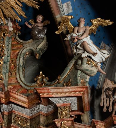 Zdjęcie nr 41: Ołtarz architektoniczny, trójosiowy, z wydzieloną częścią cokołową z bramkami bocznymi, jednokondygnacyjny, ze zwieńczeniem. Mensa drewniana z portatylem z marmuru dębnickiego, umieszczona na drewnianej, prostopadłościennej skrzyni.  Antepedium w kształcie leżącego prostokąta, ujęte profilowaną ramą dekorowaną liśćmi akantu i perełkowaniem. W polu płaskorzeźbione przedstawienie baranka leżącego na krzyżu, na obłoku, ujęte parą liści akantu oraz wicią roślinną z kwiatami i kiściami winogron. 
Na mensie tabernakulum z Tronem Łaski w formie prostopadłościanu na cokole, o wypukłej ściance frontowej, ujęte spływami wolutowymi podtrzymującymi niepełne belkowanie, wyłamane po środku łukiem półkolistym. Na froncie obrotowa nisza ujęta obramieniem w kształcie stojącego prostokąta zamkniętego łukiem nadwieszonym. W niszy ryte przedstawienie kielicha z Eucharystią w glorii, na obłoku, całość w rocaillowej ramie. Powyżej tron wystawienia z cokołem dekorowanym rocaille’em i parą ornamentalnych świeczników; ujęty parą kolumn dźwigających imposty. Podpory dżwigają rocaillowe kabłąki tworzące baldachim, na którego szczycie figurka baranka eucharystycznego leżącego na księdze. Ścianka w formie zbliżonej do stojącego prostokąta ujęta rocaille. Tabernakulum i tron ujęte okazałymi spływami wolutowymi z rocaillowymi uszami oraz na zakończeniach u dołu dwiema rzeźbami klęczących, adorujących aniołów.
Osie nastawy wydzielone w osiach skrajnych parą kolumn o skręconych trzonach i korynckich kapitelach umieszczonych na tle pilastrów, w osiach wewnętrznych parą pilastrów o trzonach w formie wolut z puttami z puttami, podtrzymywaną przez kariatydy w formie okazałych figur uskrzydlonych aniołów. Podpory wspierają pełne belkowanie z profilowanym gzymsem, występujące nad nimi, przerwane nad polem środkowym. W polu środkowym nisza ze sklepieniem kolebkowym wspartym na dwóch filarach i pilastrach. W głębi niszy obraz Św. Bartłomiej w profilowanej ramie w kształcie stojącego prostokąta zamkniętego łukiem odcinkowym. Na podniebiu niszy obraz Męczeństwo św. Bartłomieja w kształcie leżącego prostokąta ujętego niesymetrycznym obramieniem z motywem rocaille’ów. Nisza flankowana z figurami św. Stefana i św. Emeryka umieszczonymi na konsolach, na tle pilastrów. Pola retabulum w osiach skrajnych wklęsłe, między podporami prześwity z figurami św. Piotra i św. Pawła. W partii wysokiego cokołu bramki ujęte od zewnątrz wklęsłymi filarami podtrzymującymi belkowanie, wejścia z drzwiczkami w kształcie stojącego prostokąta zamkniętego łukiem półkolistym z obrazami przedstawiającymi Mojżesza i Aarona. Zwieńczenie w formie aedikuli ujętej pilastrami wspierającymi przerwane belkowanie oraz fantazyjnymi spływami wolutowymi, spływającymi na wewnętrzne podpory, przyjmując formę przerwanego przyczółka, na którym dwa putta i dwie figury siedzących aniołów. W osiach zewnętrznych podpór dwa putta siedzące kanelowanych postumentach i obłokach, prawe przytrzymuje skórę (atrybut św. Bartłomieja). W polu zwieńczenia obraz Św. Anna Samotrzeć w kształcie wydłużonego ośmioboku, w ornamentalnej ramie. Całość zwieńczona rzeźbioną półpostacią Boga Ojca pośród obłoków ukazanego w glorii promienistej. Drzwi do bramek flankowane liściastymi festonami, powyżej tarcze ujęte liśćmi laurowymi, zwieńczone koroną z klejnotem; lewa z klejnotem w postaci łabędzia z napisem: SOLI/ DEO/GLORIA, prawa z postacią ludzką z napisem: SOLI DEO HONOR. Woluty i fryz dekorowane motywami rocaille’ów oraz uskrzydlonymi główkami anielskimi. Osie boczne wypełnione ażurowymi rocaille’ami z gałązkami różanymi oraz ornamentem małżowinowo-chrząstkowym, belkowanie z podwieszonym lambrekinem z chwostami. Skręcone trzony kolumn zdobione wicią z winnej latorośli. Archiwolta nad polem środkowym dekorowana rocaille’em, rocaille’owym kartuszem i lambrekinem z chwostami. Woluty zwieńczenia, pilastry i naroża pola obrazowego dekorowane motywami rocaille’ów. 
Nastawa marmoryzowana w odcieniu jasnoszarym, profile marmoryzowane w kolorze jasnoróżowym, ornamenty i obramienia złocone.