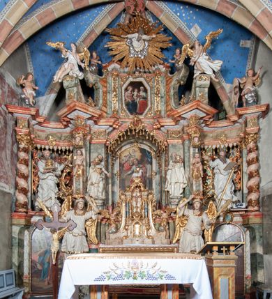 Zdjęcie nr 1: Ołtarz architektoniczny, trójosiowy, z wydzieloną częścią cokołową z bramkami bocznymi, jednokondygnacyjny, ze zwieńczeniem. Mensa drewniana z portatylem z marmuru dębnickiego, umieszczona na drewnianej, prostopadłościennej skrzyni.  Antepedium w kształcie leżącego prostokąta, ujęte profilowaną ramą dekorowaną liśćmi akantu i perełkowaniem. W polu płaskorzeźbione przedstawienie baranka leżącego na krzyżu, na obłoku, ujęte parą liści akantu oraz wicią roślinną z kwiatami i kiściami winogron. 
Na mensie tabernakulum z Tronem Łaski w formie prostopadłościanu na cokole, o wypukłej ściance frontowej, ujęte spływami wolutowymi podtrzymującymi niepełne belkowanie, wyłamane po środku łukiem półkolistym. Na froncie obrotowa nisza ujęta obramieniem w kształcie stojącego prostokąta zamkniętego łukiem nadwieszonym. W niszy ryte przedstawienie kielicha z Eucharystią w glorii, na obłoku, całość w rocaillowej ramie. Powyżej tron wystawienia z cokołem dekorowanym rocaille’em i parą ornamentalnych świeczników; ujęty parą kolumn dźwigających imposty. Podpory dżwigają rocaillowe kabłąki tworzące baldachim, na którego szczycie figurka baranka eucharystycznego leżącego na księdze. Ścianka w formie zbliżonej do stojącego prostokąta ujęta rocaille. Tabernakulum i tron ujęte okazałymi spływami wolutowymi z rocaillowymi uszami oraz na zakończeniach u dołu dwiema rzeźbami klęczących, adorujących aniołów.
Osie nastawy wydzielone w osiach skrajnych parą kolumn o skręconych trzonach i korynckich kapitelach umieszczonych na tle pilastrów, w osiach wewnętrznych parą pilastrów o trzonach w formie wolut z puttami z puttami, podtrzymywaną przez kariatydy w formie okazałych figur uskrzydlonych aniołów. Podpory wspierają pełne belkowanie z profilowanym gzymsem, występujące nad nimi, przerwane nad polem środkowym. W polu środkowym nisza ze sklepieniem kolebkowym wspartym na dwóch filarach i pilastrach. W głębi niszy obraz Św. Bartłomiej w profilowanej ramie w kształcie stojącego prostokąta zamkniętego łukiem odcinkowym. Na podniebiu niszy obraz Męczeństwo św. Bartłomieja w kształcie leżącego prostokąta ujętego niesymetrycznym obramieniem z motywem rocaille’ów. Nisza flankowana z figurami św. Stefana i św. Emeryka umieszczonymi na konsolach, na tle pilastrów. Pola retabulum w osiach skrajnych wklęsłe, między podporami prześwity z figurami św. Piotra i św. Pawła. W partii wysokiego cokołu bramki ujęte od zewnątrz wklęsłymi filarami podtrzymującymi belkowanie, wejścia z drzwiczkami w kształcie stojącego prostokąta zamkniętego łukiem półkolistym z obrazami przedstawiającymi Mojżesza i Aarona. Zwieńczenie w formie aedikuli ujętej pilastrami wspierającymi przerwane belkowanie oraz fantazyjnymi spływami wolutowymi, spływającymi na wewnętrzne podpory, przyjmując formę przerwanego przyczółka, na którym dwa putta i dwie figury siedzących aniołów. W osiach zewnętrznych podpór dwa putta siedzące kanelowanych postumentach i obłokach, prawe przytrzymuje skórę (atrybut św. Bartłomieja). W polu zwieńczenia obraz Św. Anna Samotrzeć w kształcie wydłużonego ośmioboku, w ornamentalnej ramie. Całość zwieńczona rzeźbioną półpostacią Boga Ojca pośród obłoków ukazanego w glorii promienistej. Drzwi do bramek flankowane liściastymi festonami, powyżej tarcze ujęte liśćmi laurowymi, zwieńczone koroną z klejnotem; lewa z klejnotem w postaci łabędzia z napisem: SOLI/ DEO/GLORIA, prawa z postacią ludzką z napisem: SOLI DEO HONOR. Woluty i fryz dekorowane motywami rocaille’ów oraz uskrzydlonymi główkami anielskimi. Osie boczne wypełnione ażurowymi rocaille’ami z gałązkami różanymi oraz ornamentem małżowinowo-chrząstkowym, belkowanie z podwieszonym lambrekinem z chwostami. Skręcone trzony kolumn zdobione wicią z winnej latorośli. Archiwolta nad polem środkowym dekorowana rocaille’em, rocaille’owym kartuszem i lambrekinem z chwostami. Woluty zwieńczenia, pilastry i naroża pola obrazowego dekorowane motywami rocaille’ów. 
Nastawa marmoryzowana w odcieniu jasnoszarym, profile marmoryzowane w kolorze jasnoróżowym, ornamenty i obramienia złocone.