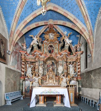 Zdjęcie nr 5: Ołtarz architektoniczny, trójosiowy, z wydzieloną częścią cokołową z bramkami bocznymi, jednokondygnacyjny, ze zwieńczeniem. Mensa drewniana z portatylem z marmuru dębnickiego, umieszczona na drewnianej, prostopadłościennej skrzyni.  Antepedium w kształcie leżącego prostokąta, ujęte profilowaną ramą dekorowaną liśćmi akantu i perełkowaniem. W polu płaskorzeźbione przedstawienie baranka leżącego na krzyżu, na obłoku, ujęte parą liści akantu oraz wicią roślinną z kwiatami i kiściami winogron. 
Na mensie tabernakulum z Tronem Łaski w formie prostopadłościanu na cokole, o wypukłej ściance frontowej, ujęte spływami wolutowymi podtrzymującymi niepełne belkowanie, wyłamane po środku łukiem półkolistym. Na froncie obrotowa nisza ujęta obramieniem w kształcie stojącego prostokąta zamkniętego łukiem nadwieszonym. W niszy ryte przedstawienie kielicha z Eucharystią w glorii, na obłoku, całość w rocaillowej ramie. Powyżej tron wystawienia z cokołem dekorowanym rocaille’em i parą ornamentalnych świeczników; ujęty parą kolumn dźwigających imposty. Podpory dżwigają rocaillowe kabłąki tworzące baldachim, na którego szczycie figurka baranka eucharystycznego leżącego na księdze. Ścianka w formie zbliżonej do stojącego prostokąta ujęta rocaille. Tabernakulum i tron ujęte okazałymi spływami wolutowymi z rocaillowymi uszami oraz na zakończeniach u dołu dwiema rzeźbami klęczących, adorujących aniołów.
Osie nastawy wydzielone w osiach skrajnych parą kolumn o skręconych trzonach i korynckich kapitelach umieszczonych na tle pilastrów, w osiach wewnętrznych parą pilastrów o trzonach w formie wolut z puttami z puttami, podtrzymywaną przez kariatydy w formie okazałych figur uskrzydlonych aniołów. Podpory wspierają pełne belkowanie z profilowanym gzymsem, występujące nad nimi, przerwane nad polem środkowym. W polu środkowym nisza ze sklepieniem kolebkowym wspartym na dwóch filarach i pilastrach. W głębi niszy obraz Św. Bartłomiej w profilowanej ramie w kształcie stojącego prostokąta zamkniętego łukiem odcinkowym. Na podniebiu niszy obraz Męczeństwo św. Bartłomieja w kształcie leżącego prostokąta ujętego niesymetrycznym obramieniem z motywem rocaille’ów. Nisza flankowana z figurami św. Stefana i św. Emeryka umieszczonymi na konsolach, na tle pilastrów. Pola retabulum w osiach skrajnych wklęsłe, między podporami prześwity z figurami św. Piotra i św. Pawła. W partii wysokiego cokołu bramki ujęte od zewnątrz wklęsłymi filarami podtrzymującymi belkowanie, wejścia z drzwiczkami w kształcie stojącego prostokąta zamkniętego łukiem półkolistym z obrazami przedstawiającymi Mojżesza i Aarona. Zwieńczenie w formie aedikuli ujętej pilastrami wspierającymi przerwane belkowanie oraz fantazyjnymi spływami wolutowymi, spływającymi na wewnętrzne podpory, przyjmując formę przerwanego przyczółka, na którym dwa putta i dwie figury siedzących aniołów. W osiach zewnętrznych podpór dwa putta siedzące kanelowanych postumentach i obłokach, prawe przytrzymuje skórę (atrybut św. Bartłomieja). W polu zwieńczenia obraz Św. Anna Samotrzeć w kształcie wydłużonego ośmioboku, w ornamentalnej ramie. Całość zwieńczona rzeźbioną półpostacią Boga Ojca pośród obłoków ukazanego w glorii promienistej. Drzwi do bramek flankowane liściastymi festonami, powyżej tarcze ujęte liśćmi laurowymi, zwieńczone koroną z klejnotem; lewa z klejnotem w postaci łabędzia z napisem: SOLI/ DEO/GLORIA, prawa z postacią ludzką z napisem: SOLI DEO HONOR. Woluty i fryz dekorowane motywami rocaille’ów oraz uskrzydlonymi główkami anielskimi. Osie boczne wypełnione ażurowymi rocaille’ami z gałązkami różanymi oraz ornamentem małżowinowo-chrząstkowym, belkowanie z podwieszonym lambrekinem z chwostami. Skręcone trzony kolumn zdobione wicią z winnej latorośli. Archiwolta nad polem środkowym dekorowana rocaille’em, rocaille’owym kartuszem i lambrekinem z chwostami. Woluty zwieńczenia, pilastry i naroża pola obrazowego dekorowane motywami rocaille’ów. 
Nastawa marmoryzowana w odcieniu jasnoszarym, profile marmoryzowane w kolorze jasnoróżowym, ornamenty i obramienia złocone.