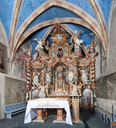 Zdjęcie nr 8: Ołtarz architektoniczny, trójosiowy, z wydzieloną częścią cokołową z bramkami bocznymi, jednokondygnacyjny, ze zwieńczeniem. Mensa drewniana z portatylem z marmuru dębnickiego, umieszczona na drewnianej, prostopadłościennej skrzyni.  Antepedium w kształcie leżącego prostokąta, ujęte profilowaną ramą dekorowaną liśćmi akantu i perełkowaniem. W polu płaskorzeźbione przedstawienie baranka leżącego na krzyżu, na obłoku, ujęte parą liści akantu oraz wicią roślinną z kwiatami i kiściami winogron. 
Na mensie tabernakulum z Tronem Łaski w formie prostopadłościanu na cokole, o wypukłej ściance frontowej, ujęte spływami wolutowymi podtrzymującymi niepełne belkowanie, wyłamane po środku łukiem półkolistym. Na froncie obrotowa nisza ujęta obramieniem w kształcie stojącego prostokąta zamkniętego łukiem nadwieszonym. W niszy ryte przedstawienie kielicha z Eucharystią w glorii, na obłoku, całość w rocaillowej ramie. Powyżej tron wystawienia z cokołem dekorowanym rocaille’em i parą ornamentalnych świeczników; ujęty parą kolumn dźwigających imposty. Podpory dżwigają rocaillowe kabłąki tworzące baldachim, na którego szczycie figurka baranka eucharystycznego leżącego na księdze. Ścianka w formie zbliżonej do stojącego prostokąta ujęta rocaille. Tabernakulum i tron ujęte okazałymi spływami wolutowymi z rocaillowymi uszami oraz na zakończeniach u dołu dwiema rzeźbami klęczących, adorujących aniołów.
Osie nastawy wydzielone w osiach skrajnych parą kolumn o skręconych trzonach i korynckich kapitelach umieszczonych na tle pilastrów, w osiach wewnętrznych parą pilastrów o trzonach w formie wolut z puttami z puttami, podtrzymywaną przez kariatydy w formie okazałych figur uskrzydlonych aniołów. Podpory wspierają pełne belkowanie z profilowanym gzymsem, występujące nad nimi, przerwane nad polem środkowym. W polu środkowym nisza ze sklepieniem kolebkowym wspartym na dwóch filarach i pilastrach. W głębi niszy obraz Św. Bartłomiej w profilowanej ramie w kształcie stojącego prostokąta zamkniętego łukiem odcinkowym. Na podniebiu niszy obraz Męczeństwo św. Bartłomieja w kształcie leżącego prostokąta ujętego niesymetrycznym obramieniem z motywem rocaille’ów. Nisza flankowana z figurami św. Stefana i św. Emeryka umieszczonymi na konsolach, na tle pilastrów. Pola retabulum w osiach skrajnych wklęsłe, między podporami prześwity z figurami św. Piotra i św. Pawła. W partii wysokiego cokołu bramki ujęte od zewnątrz wklęsłymi filarami podtrzymującymi belkowanie, wejścia z drzwiczkami w kształcie stojącego prostokąta zamkniętego łukiem półkolistym z obrazami przedstawiającymi Mojżesza i Aarona. Zwieńczenie w formie aedikuli ujętej pilastrami wspierającymi przerwane belkowanie oraz fantazyjnymi spływami wolutowymi, spływającymi na wewnętrzne podpory, przyjmując formę przerwanego przyczółka, na którym dwa putta i dwie figury siedzących aniołów. W osiach zewnętrznych podpór dwa putta siedzące kanelowanych postumentach i obłokach, prawe przytrzymuje skórę (atrybut św. Bartłomieja). W polu zwieńczenia obraz Św. Anna Samotrzeć w kształcie wydłużonego ośmioboku, w ornamentalnej ramie. Całość zwieńczona rzeźbioną półpostacią Boga Ojca pośród obłoków ukazanego w glorii promienistej. Drzwi do bramek flankowane liściastymi festonami, powyżej tarcze ujęte liśćmi laurowymi, zwieńczone koroną z klejnotem; lewa z klejnotem w postaci łabędzia z napisem: SOLI/ DEO/GLORIA, prawa z postacią ludzką z napisem: SOLI DEO HONOR. Woluty i fryz dekorowane motywami rocaille’ów oraz uskrzydlonymi główkami anielskimi. Osie boczne wypełnione ażurowymi rocaille’ami z gałązkami różanymi oraz ornamentem małżowinowo-chrząstkowym, belkowanie z podwieszonym lambrekinem z chwostami. Skręcone trzony kolumn zdobione wicią z winnej latorośli. Archiwolta nad polem środkowym dekorowana rocaille’em, rocaille’owym kartuszem i lambrekinem z chwostami. Woluty zwieńczenia, pilastry i naroża pola obrazowego dekorowane motywami rocaille’ów. 
Nastawa marmoryzowana w odcieniu jasnoszarym, profile marmoryzowane w kolorze jasnoróżowym, ornamenty i obramienia złocone.