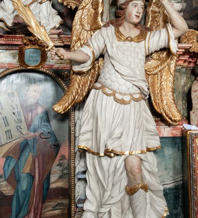 Zdjęcie nr 48: Ołtarz architektoniczny, trójosiowy, z wydzieloną częścią cokołową z bramkami bocznymi, jednokondygnacyjny, ze zwieńczeniem. Mensa drewniana z portatylem z marmuru dębnickiego, umieszczona na drewnianej, prostopadłościennej skrzyni.  Antepedium w kształcie leżącego prostokąta, ujęte profilowaną ramą dekorowaną liśćmi akantu i perełkowaniem. W polu płaskorzeźbione przedstawienie baranka leżącego na krzyżu, na obłoku, ujęte parą liści akantu oraz wicią roślinną z kwiatami i kiściami winogron. 
Na mensie tabernakulum z Tronem Łaski w formie prostopadłościanu na cokole, o wypukłej ściance frontowej, ujęte spływami wolutowymi podtrzymującymi niepełne belkowanie, wyłamane po środku łukiem półkolistym. Na froncie obrotowa nisza ujęta obramieniem w kształcie stojącego prostokąta zamkniętego łukiem nadwieszonym. W niszy ryte przedstawienie kielicha z Eucharystią w glorii, na obłoku, całość w rocaillowej ramie. Powyżej tron wystawienia z cokołem dekorowanym rocaille’em i parą ornamentalnych świeczników; ujęty parą kolumn dźwigających imposty. Podpory dżwigają rocaillowe kabłąki tworzące baldachim, na którego szczycie figurka baranka eucharystycznego leżącego na księdze. Ścianka w formie zbliżonej do stojącego prostokąta ujęta rocaille. Tabernakulum i tron ujęte okazałymi spływami wolutowymi z rocaillowymi uszami oraz na zakończeniach u dołu dwiema rzeźbami klęczących, adorujących aniołów.
Osie nastawy wydzielone w osiach skrajnych parą kolumn o skręconych trzonach i korynckich kapitelach umieszczonych na tle pilastrów, w osiach wewnętrznych parą pilastrów o trzonach w formie wolut z puttami z puttami, podtrzymywaną przez kariatydy w formie okazałych figur uskrzydlonych aniołów. Podpory wspierają pełne belkowanie z profilowanym gzymsem, występujące nad nimi, przerwane nad polem środkowym. W polu środkowym nisza ze sklepieniem kolebkowym wspartym na dwóch filarach i pilastrach. W głębi niszy obraz Św. Bartłomiej w profilowanej ramie w kształcie stojącego prostokąta zamkniętego łukiem odcinkowym. Na podniebiu niszy obraz Męczeństwo św. Bartłomieja w kształcie leżącego prostokąta ujętego niesymetrycznym obramieniem z motywem rocaille’ów. Nisza flankowana z figurami św. Stefana i św. Emeryka umieszczonymi na konsolach, na tle pilastrów. Pola retabulum w osiach skrajnych wklęsłe, między podporami prześwity z figurami św. Piotra i św. Pawła. W partii wysokiego cokołu bramki ujęte od zewnątrz wklęsłymi filarami podtrzymującymi belkowanie, wejścia z drzwiczkami w kształcie stojącego prostokąta zamkniętego łukiem półkolistym z obrazami przedstawiającymi Mojżesza i Aarona. Zwieńczenie w formie aedikuli ujętej pilastrami wspierającymi przerwane belkowanie oraz fantazyjnymi spływami wolutowymi, spływającymi na wewnętrzne podpory, przyjmując formę przerwanego przyczółka, na którym dwa putta i dwie figury siedzących aniołów. W osiach zewnętrznych podpór dwa putta siedzące kanelowanych postumentach i obłokach, prawe przytrzymuje skórę (atrybut św. Bartłomieja). W polu zwieńczenia obraz Św. Anna Samotrzeć w kształcie wydłużonego ośmioboku, w ornamentalnej ramie. Całość zwieńczona rzeźbioną półpostacią Boga Ojca pośród obłoków ukazanego w glorii promienistej. Drzwi do bramek flankowane liściastymi festonami, powyżej tarcze ujęte liśćmi laurowymi, zwieńczone koroną z klejnotem; lewa z klejnotem w postaci łabędzia z napisem: SOLI/ DEO/GLORIA, prawa z postacią ludzką z napisem: SOLI DEO HONOR. Woluty i fryz dekorowane motywami rocaille’ów oraz uskrzydlonymi główkami anielskimi. Osie boczne wypełnione ażurowymi rocaille’ami z gałązkami różanymi oraz ornamentem małżowinowo-chrząstkowym, belkowanie z podwieszonym lambrekinem z chwostami. Skręcone trzony kolumn zdobione wicią z winnej latorośli. Archiwolta nad polem środkowym dekorowana rocaille’em, rocaille’owym kartuszem i lambrekinem z chwostami. Woluty zwieńczenia, pilastry i naroża pola obrazowego dekorowane motywami rocaille’ów. 
Nastawa marmoryzowana w odcieniu jasnoszarym, profile marmoryzowane w kolorze jasnoróżowym, ornamenty i obramienia złocone.