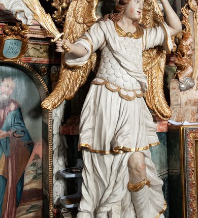 Zdjęcie nr 47: Ołtarz architektoniczny, trójosiowy, z wydzieloną częścią cokołową z bramkami bocznymi, jednokondygnacyjny, ze zwieńczeniem. Mensa drewniana z portatylem z marmuru dębnickiego, umieszczona na drewnianej, prostopadłościennej skrzyni.  Antepedium w kształcie leżącego prostokąta, ujęte profilowaną ramą dekorowaną liśćmi akantu i perełkowaniem. W polu płaskorzeźbione przedstawienie baranka leżącego na krzyżu, na obłoku, ujęte parą liści akantu oraz wicią roślinną z kwiatami i kiściami winogron. 
Na mensie tabernakulum z Tronem Łaski w formie prostopadłościanu na cokole, o wypukłej ściance frontowej, ujęte spływami wolutowymi podtrzymującymi niepełne belkowanie, wyłamane po środku łukiem półkolistym. Na froncie obrotowa nisza ujęta obramieniem w kształcie stojącego prostokąta zamkniętego łukiem nadwieszonym. W niszy ryte przedstawienie kielicha z Eucharystią w glorii, na obłoku, całość w rocaillowej ramie. Powyżej tron wystawienia z cokołem dekorowanym rocaille’em i parą ornamentalnych świeczników; ujęty parą kolumn dźwigających imposty. Podpory dżwigają rocaillowe kabłąki tworzące baldachim, na którego szczycie figurka baranka eucharystycznego leżącego na księdze. Ścianka w formie zbliżonej do stojącego prostokąta ujęta rocaille. Tabernakulum i tron ujęte okazałymi spływami wolutowymi z rocaillowymi uszami oraz na zakończeniach u dołu dwiema rzeźbami klęczących, adorujących aniołów.
Osie nastawy wydzielone w osiach skrajnych parą kolumn o skręconych trzonach i korynckich kapitelach umieszczonych na tle pilastrów, w osiach wewnętrznych parą pilastrów o trzonach w formie wolut z puttami z puttami, podtrzymywaną przez kariatydy w formie okazałych figur uskrzydlonych aniołów. Podpory wspierają pełne belkowanie z profilowanym gzymsem, występujące nad nimi, przerwane nad polem środkowym. W polu środkowym nisza ze sklepieniem kolebkowym wspartym na dwóch filarach i pilastrach. W głębi niszy obraz Św. Bartłomiej w profilowanej ramie w kształcie stojącego prostokąta zamkniętego łukiem odcinkowym. Na podniebiu niszy obraz Męczeństwo św. Bartłomieja w kształcie leżącego prostokąta ujętego niesymetrycznym obramieniem z motywem rocaille’ów. Nisza flankowana z figurami św. Stefana i św. Emeryka umieszczonymi na konsolach, na tle pilastrów. Pola retabulum w osiach skrajnych wklęsłe, między podporami prześwity z figurami św. Piotra i św. Pawła. W partii wysokiego cokołu bramki ujęte od zewnątrz wklęsłymi filarami podtrzymującymi belkowanie, wejścia z drzwiczkami w kształcie stojącego prostokąta zamkniętego łukiem półkolistym z obrazami przedstawiającymi Mojżesza i Aarona. Zwieńczenie w formie aedikuli ujętej pilastrami wspierającymi przerwane belkowanie oraz fantazyjnymi spływami wolutowymi, spływającymi na wewnętrzne podpory, przyjmując formę przerwanego przyczółka, na którym dwa putta i dwie figury siedzących aniołów. W osiach zewnętrznych podpór dwa putta siedzące kanelowanych postumentach i obłokach, prawe przytrzymuje skórę (atrybut św. Bartłomieja). W polu zwieńczenia obraz Św. Anna Samotrzeć w kształcie wydłużonego ośmioboku, w ornamentalnej ramie. Całość zwieńczona rzeźbioną półpostacią Boga Ojca pośród obłoków ukazanego w glorii promienistej. Drzwi do bramek flankowane liściastymi festonami, powyżej tarcze ujęte liśćmi laurowymi, zwieńczone koroną z klejnotem; lewa z klejnotem w postaci łabędzia z napisem: SOLI/ DEO/GLORIA, prawa z postacią ludzką z napisem: SOLI DEO HONOR. Woluty i fryz dekorowane motywami rocaille’ów oraz uskrzydlonymi główkami anielskimi. Osie boczne wypełnione ażurowymi rocaille’ami z gałązkami różanymi oraz ornamentem małżowinowo-chrząstkowym, belkowanie z podwieszonym lambrekinem z chwostami. Skręcone trzony kolumn zdobione wicią z winnej latorośli. Archiwolta nad polem środkowym dekorowana rocaille’em, rocaille’owym kartuszem i lambrekinem z chwostami. Woluty zwieńczenia, pilastry i naroża pola obrazowego dekorowane motywami rocaille’ów. 
Nastawa marmoryzowana w odcieniu jasnoszarym, profile marmoryzowane w kolorze jasnoróżowym, ornamenty i obramienia złocone.