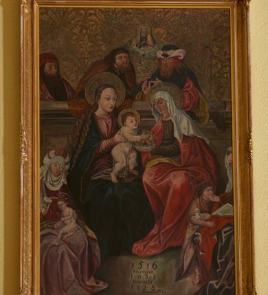 Zdjęcie nr 3: Obraz w formie stojącego prostokąta w drewnianej, profilowanej, złoconej i fakturowanej ramie, w narożach i pośrodku boków zdobionej wicią stylizowanego rocaille&#039;u. W centrum kompozycja przedstawiająca rodzinę Matki Boskiej w ujęciu dwustrefowym. W centrum umieszczona grupa z siedzącymi na ławie Matką Boską z Dzieciątkiem, zwróconą trzy czwarte w lewo oraz św. Anną zwróconą trzy czwarte w prawo. Maria dwiema wyciągniętymi przed siebie rękami przytrzymuje stojące na jej kolanach Dzieciątko. Matka Boska ma owalną twarz z wysokim czołem, zadartym nosem, małymi ustami i oczami. Głowę okalają bardzo długie, bujne włosy, opadające falami na ramiona i podwiązane wąska opaską. Ubrana jest w czerwoną suknię z długim rękawem oraz granatowy płaszcz ze złotą lamówką. Dzieciątko zwrócone jest trzy czwarte w lewo, ma podkulone nóżki, dłońmi sięga po owoce, które na półmisku trzyma św. Anna. Twarz okrągła o pucułowatych policzkach z wyraźnie zaznaczonym podbródkiem. Włosy krótkie, jasne z loczkiem pośrodku czoła. Ubrane jest w długą, przezroczystą sukienkę. Święta Anna ma twarz o wyrazistych rysach. Ubrana jest w oliwkową suknię z długimi rękawami, czerwony płaszcz z żółtą podszewką i biały welon na głowie. Cała trójka ma wokół głów złote i tłoczone nimby. W lewym dolnym narożu obrazu siedzi Maria Salome z małym św. Janem Ewangelistą na kolanach. Maria ubrana jest w czerwoną suknię i fioletowy płaszcz, ma również białą podwikę z welonem i czepcem na głowie. W prawej dłoni trzyma białą różę. Święty Jan ukazany został jako małe dziecko z kielichem w dłoniach, z którego wyłania się wąż. Dziecko ubrane jest w białą pieluszkę, odsłaniającą nagie ramiona i klatkę piersiową. Po prawej stronie obrazu jest ucięta postać św. Elżbiety, zwrócona trzy czwarte w prawo, która wyciąga dłoń ku stojącemu obok młodzieńczemu św. Janowi Chrzcicielowi. Święta ubrana jest w brązową suknię oraz fioletowy płaszcz z czerwoną podszewką. Na głowie ma biały welon spięty ozdobną opaską z klejnotami, a na kolanach trzyma otwartą księgę. Święty Jan Chrzciciel zwrócony jest w stronę Matki. Na prawej ręce trzyma małego białego baranka oraz prosty krzyż. Ubrany jest w skórę z sierści wielbłąda. Nad głowami Marii Salome, św. Jana Ewangelisty, św. Elżbiety oraz św. Jana Chrzciciela znajdują się złote i okrągłe nimby. W górnej strefie obrazu za wysoką ławą stoją kolejno od lewej: Zebedeusz, św. Józef oraz św. Joachim. Zebedeusz ubrany jest w ciemnozieloną suknię, jasnofioletowy płaszcz oraz czerwoną czapkę; św. Józef ma ciemnofioletową suknię z białym kołnierzykiem i brązowy płaszcz; św. Joachim ma czerwoną suknię, zielony płaszcz z żółtą podszewką oraz  trójkolorowe nakrycie głowy. Wszyscy mężczyźni mają twarze ukazujące ich w sile wieku, okolone bujnymi brązowymi brodami. Pomiędzy św. Józefem, a św. Joachimem, wyłania się spośród obłoków niewielkie popiersie błogosławiącego Boga Ojca i gołębica Ducha Świętego. Tło obrazu złocone i tłoczone w motywy roślinne. U dołu inskrypcja: „1516 / RENOVATVM / 1638 / RENOVATVM / 1825 / RENOVATVM 1921”.