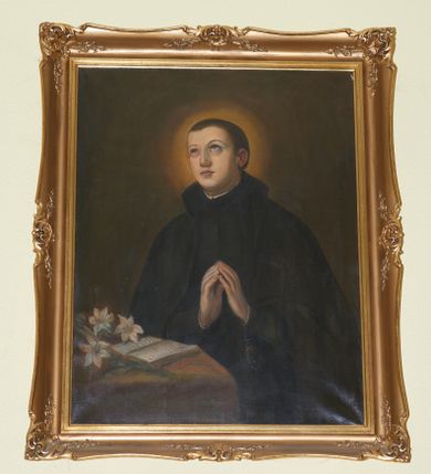 Zdjęcie nr 1: Obraz w kształcie stojącego prostokąta w profilowanej, złoconej ramie. W centrum kompozycji ukazany w półpostaci modlący się św. Stanisław Kostka. Święty unosi głowę i wzrok ku górze, ręce składa w geście modlitwy. Twarz młodzieńcza, o owalnym kształcie, długi i prosty nos, małe usta, bardzo krótkie, ciemnobrązowe włosy. Ubrany jest w czarną sutannę oraz płaszcz. Na lewej dłoni ma zawieszony różaniec, a wokół głowy świetlisty, złoty nimb. Przed nim, na stole leży otwarta księga oraz kwiaty białych lilii. Tło jednolicie brązowe. Kolorystyka ciemna, przygaszona.