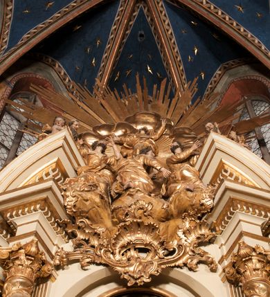 Zdjęcie nr 32: Nastawa jednoosiowa, jednokondygnacyjna ze zwieńczeniem, na wysokim dwustrefowym cokole z wyodrębnionymi czterema prostopadłościanami. Ołtarz kamienny, prostopadłościenny, z kamienną mensą. Antepedium ujęte srebrzoną opaską z napisem „kości ich niech wypuszczą pędu ze swego miejsca, aby byli wsławieni przez swoich synów”, pole podzielone na cztery części ornamentem roślinnym, każda wypełniona złoconą wicią kwiatową i czterema okrągłymi prześwitami. Na ołtarzu ustawione tabernakulum w formie Arki Przymierza. Nastawa ujęta dwiema parami pilastrów i dwiema parami kolumn o kręconych trzonach ustawionych pod kątem na zewnątrz, dźwigającymi pełne belkowanie z kostkowaniem, wyłamane na ich osi, przerwane nad polem środkowym oraz fragmenty przerwanego, półkolistego przyczółka. W polu środkowym wnęka w formie stojącego prostokąta zamkniętego łukiem półkolistym, w niej mniejszy obraz w kształcie stojącego prostokąta zamkniętego łukiem półkolistym nadwieszonym z przedstawieniem Wizji św. Franciszka, ujęty ramą dekorowaną rocaille'em. Zwieńczenie w formie grupy rzeźbiarskiej Przemienienia Pańskiego na tle obłoków i w glorii promienistej. 
W partii belkowania nad polem głównym, na rzeźbionej skale podtrzymywanej przez rocaille klęczące postacie św. Piotra, św. Jana i św. Jakuba w dynamicznych pozach. Nad nimi unosi się Chrystus w otoku z obłoków i glorii, flankowany przez figury Mojżesza i Eliasza klęczące na przerwanym przyczółku, za nimi nadlatujące putta na obłokach. Po lewej stronie Piotr klęczący frontalnie z uniesionymi rękami. Obok niego klęczący św. Jan zwrócony profilem w lewo, z rękami wyciągniętymi w przód, o młodzieńczych rysach i długich, kręconych włosach. Święty Jakub po prawej stronie, w pozycji siedzącej, zwrócony w trzech czwartych w prawo z rękami wyciągniętymi w lewo. Wszyscy ubrani w przylegające do ciała tuniki oraz płaszcze przepasane w partii nóg. Nad nimi Chrystus w pozycji stojącej, frontalnie, w kontrapoście, z uniesioną głową i rękami rozłożonymi na boki, ubrany jest w tunikę oraz płaszcz przewiązany przez lewe ramię i wokół nóg. Na lewym fragmencie przyczółka klęczy Eliasz, zwrócony w trzech czwartych w lewo, pochylony, prawą ręką przytrzymuje na boku księgę, lewą wyciąga w przód. Ubrany jest w tunikę oraz rozwiany płaszcz. Na prawym fragmencie przyczółka klęczy Mojżesz, zwrócony w trzech czwartych w prawo, z pochylona głową, obiema rękami trzyma tablice przykazań. Ubrany jest w tunikę o krótkich rękawach oraz płaszcz zawinięty na lewym ramieniu i opadający na nogi. Obaj prorocy ukazani jako starcy. Nastawa flankowana dwoma wspornikami z figurami św. Wacława i św. Floriana. Struktura polichromowana w kolorze beżowym z żółtymi detalami oraz złoconymi profilami, ornamentyką i zwieńczeniem. Figury w partii ciała polichromowane naturalistycznie z brązowymi włosami i brodami oraz złoconymi szatami i atrybutami. 

