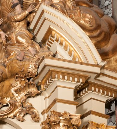 Zdjęcie nr 37: Nastawa jednoosiowa, jednokondygnacyjna ze zwieńczeniem, na wysokim dwustrefowym cokole z wyodrębnionymi czterema prostopadłościanami. Ołtarz kamienny, prostopadłościenny, z kamienną mensą. Antepedium ujęte srebrzoną opaską z napisem „kości ich niech wypuszczą pędu ze swego miejsca, aby byli wsławieni przez swoich synów”, pole podzielone na cztery części ornamentem roślinnym, każda wypełniona złoconą wicią kwiatową i czterema okrągłymi prześwitami. Na ołtarzu ustawione tabernakulum w formie Arki Przymierza. Nastawa ujęta dwiema parami pilastrów i dwiema parami kolumn o kręconych trzonach ustawionych pod kątem na zewnątrz, dźwigającymi pełne belkowanie z kostkowaniem, wyłamane na ich osi, przerwane nad polem środkowym oraz fragmenty przerwanego, półkolistego przyczółka. W polu środkowym wnęka w formie stojącego prostokąta zamkniętego łukiem półkolistym, w niej mniejszy obraz w kształcie stojącego prostokąta zamkniętego łukiem półkolistym nadwieszonym z przedstawieniem Wizji św. Franciszka, ujęty ramą dekorowaną rocaille&#039;em. Zwieńczenie w formie grupy rzeźbiarskiej Przemienienia Pańskiego na tle obłoków i w glorii promienistej. 
W partii belkowania nad polem głównym, na rzeźbionej skale podtrzymywanej przez rocaille klęczące postacie św. Piotra, św. Jana i św. Jakuba w dynamicznych pozach. Nad nimi unosi się Chrystus w otoku z obłoków i glorii, flankowany przez figury Mojżesza i Eliasza klęczące na przerwanym przyczółku, za nimi nadlatujące putta na obłokach. Po lewej stronie Piotr klęczący frontalnie z uniesionymi rękami. Obok niego klęczący św. Jan zwrócony profilem w lewo, z rękami wyciągniętymi w przód, o młodzieńczych rysach i długich, kręconych włosach. Święty Jakub po prawej stronie, w pozycji siedzącej, zwrócony w trzech czwartych w prawo z rękami wyciągniętymi w lewo. Wszyscy ubrani w przylegające do ciała tuniki oraz płaszcze przepasane w partii nóg. Nad nimi Chrystus w pozycji stojącej, frontalnie, w kontrapoście, z uniesioną głową i rękami rozłożonymi na boki, ubrany jest w tunikę oraz płaszcz przewiązany przez lewe ramię i wokół nóg. Na lewym fragmencie przyczółka klęczy Eliasz, zwrócony w trzech czwartych w lewo, pochylony, prawą ręką przytrzymuje na boku księgę, lewą wyciąga w przód. Ubrany jest w tunikę oraz rozwiany płaszcz. Na prawym fragmencie przyczółka klęczy Mojżesz, zwrócony w trzech czwartych w prawo, z pochylona głową, obiema rękami trzyma tablice przykazań. Ubrany jest w tunikę o krótkich rękawach oraz płaszcz zawinięty na lewym ramieniu i opadający na nogi. Obaj prorocy ukazani jako starcy. Nastawa flankowana dwoma wspornikami z figurami św. Wacława i św. Floriana. Struktura polichromowana w kolorze beżowym z żółtymi detalami oraz złoconymi profilami, ornamentyką i zwieńczeniem. Figury w partii ciała polichromowane naturalistycznie z brązowymi włosami i brodami oraz złoconymi szatami i atrybutami. 

