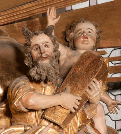 Zdjęcie nr 57: Nastawa jednoosiowa, jednokondygnacyjna ze zwieńczeniem, na wysokim dwustrefowym cokole z wyodrębnionymi czterema prostopadłościanami. Ołtarz kamienny, prostopadłościenny, z kamienną mensą. Antepedium ujęte srebrzoną opaską z napisem „kości ich niech wypuszczą pędu ze swego miejsca, aby byli wsławieni przez swoich synów”, pole podzielone na cztery części ornamentem roślinnym, każda wypełniona złoconą wicią kwiatową i czterema okrągłymi prześwitami. Na ołtarzu ustawione tabernakulum w formie Arki Przymierza. Nastawa ujęta dwiema parami pilastrów i dwiema parami kolumn o kręconych trzonach ustawionych pod kątem na zewnątrz, dźwigającymi pełne belkowanie z kostkowaniem, wyłamane na ich osi, przerwane nad polem środkowym oraz fragmenty przerwanego, półkolistego przyczółka. W polu środkowym wnęka w formie stojącego prostokąta zamkniętego łukiem półkolistym, w niej mniejszy obraz w kształcie stojącego prostokąta zamkniętego łukiem półkolistym nadwieszonym z przedstawieniem Wizji św. Franciszka, ujęty ramą dekorowaną rocaille'em. Zwieńczenie w formie grupy rzeźbiarskiej Przemienienia Pańskiego na tle obłoków i w glorii promienistej. 
W partii belkowania nad polem głównym, na rzeźbionej skale podtrzymywanej przez rocaille klęczące postacie św. Piotra, św. Jana i św. Jakuba w dynamicznych pozach. Nad nimi unosi się Chrystus w otoku z obłoków i glorii, flankowany przez figury Mojżesza i Eliasza klęczące na przerwanym przyczółku, za nimi nadlatujące putta na obłokach. Po lewej stronie Piotr klęczący frontalnie z uniesionymi rękami. Obok niego klęczący św. Jan zwrócony profilem w lewo, z rękami wyciągniętymi w przód, o młodzieńczych rysach i długich, kręconych włosach. Święty Jakub po prawej stronie, w pozycji siedzącej, zwrócony w trzech czwartych w prawo z rękami wyciągniętymi w lewo. Wszyscy ubrani w przylegające do ciała tuniki oraz płaszcze przepasane w partii nóg. Nad nimi Chrystus w pozycji stojącej, frontalnie, w kontrapoście, z uniesioną głową i rękami rozłożonymi na boki, ubrany jest w tunikę oraz płaszcz przewiązany przez lewe ramię i wokół nóg. Na lewym fragmencie przyczółka klęczy Eliasz, zwrócony w trzech czwartych w lewo, pochylony, prawą ręką przytrzymuje na boku księgę, lewą wyciąga w przód. Ubrany jest w tunikę oraz rozwiany płaszcz. Na prawym fragmencie przyczółka klęczy Mojżesz, zwrócony w trzech czwartych w prawo, z pochylona głową, obiema rękami trzyma tablice przykazań. Ubrany jest w tunikę o krótkich rękawach oraz płaszcz zawinięty na lewym ramieniu i opadający na nogi. Obaj prorocy ukazani jako starcy. Nastawa flankowana dwoma wspornikami z figurami św. Wacława i św. Floriana. Struktura polichromowana w kolorze beżowym z żółtymi detalami oraz złoconymi profilami, ornamentyką i zwieńczeniem. Figury w partii ciała polichromowane naturalistycznie z brązowymi włosami i brodami oraz złoconymi szatami i atrybutami. 

