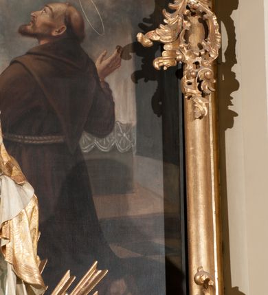 Zdjęcie nr 13: Obraz klęczącego przed ołtarzem św. Franciszka, któremu ukazuje się siedzący w chmurach Jezus i Maria w otoczeniu aniołów. Maria zwrócona w trzech czwartych w lewo, ukazana w różowej sukni, niebieskim płaszczu i z białym welonem na głowie oraz wieńcem z gwiazd. Prawa ręka wyciągnięta w stronę świętego, lewa przyłożona do piersi. Chrystus o długich, brązowych włosach i krótkim zaroście, ukazany frontalnie, w białej luźniej szacie i czerwonym płaszczu spiętym broszą i z krzyżowym promienistym nimbem nad głową. Lewa ręka lekko uniesiona do góry, prawa spoczywa na kolanie. Święty Franciszek ukazany tyłem do widza, z twarzą z profilu, uniesioną w stronę Marii, z rozłożonymi rękoma. Ubrany w brązowy habit franciszkański, przepasany podwójnym sznurem. Wokół Marii i Jezusa aniołowie w różnych pozach i główki aniołów. 