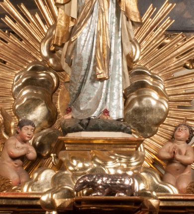 Zdjęcie nr 1: Tabernakulum w formie Arki Przymierza, adorowanej przez dwie klęczące figury starotestamentowego arcykapłana i biskupa oraz dwie stojące postacie lewitów oraz klęczące aniołów, zwieńczonej glorią promienistą z okiem Opatrzności. Wsparte na ośmiu cylindrycznych nóżkach prostopadłościenne tabernakulum jest od frontu podzielone na trzy pola wyznaczone kanelowanymi listwami. Pole środkowe stanowią drzwiczki z rytymi cyframi Dekalogu z ukrzyżowanym Chrystusem, pola boczne z wiązką pałek wodnych z jednej i winnym gronem z drugiej strony. Na skłębionych chmurach z podestem leży Baranek (obecnie w jego miejscu znajduje się figura Matki Boskiej). W tle znacznej wielkości gloria promienista z wieńcem chmur i umieszczonym w nim okiem Opatrzności oraz dwie uskrzydlone główki, nad którymi papieska tiara ze skrzyżowanymi kluczami. Po bokach Baranka dwa klęczące, uskrzydlone nagie aniołki. Obok tabernakulum dwie klęczące postacie z kadzielnicami w rękach. Postać po lewej w stroju biskupim, w albie, stule i kapie oraz infule z dwiema taśmami. Postać po prawej stronie jest ubrany w tradycyjny starotestamentowy strój – efod czyli tunikę i płaszcz wierzchni przepasany na biodrach, pektorał na piersi i zawój na głowie. Za nimi dwaj stojący lewici w tunikach przepasanych na biodrach i wysokich butach. Adorujące Baranka anioły w pozycji klęczącej z rękami skrzyżowanymi na piersi, ze skrzydłami na plecach i nogami w połowie utworzonymi ze skrzydeł.  


