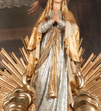 Zdjęcie nr 95: Tabernakulum w formie Arki Przymierza, adorowanej przez dwie klęczące figury starotestamentowego arcykapłana i biskupa oraz dwie stojące postacie lewitów oraz klęczące aniołów, zwieńczonej glorią promienistą z okiem Opatrzności. Wsparte na ośmiu cylindrycznych nóżkach prostopadłościenne tabernakulum jest od frontu podzielone na trzy pola wyznaczone kanelowanymi listwami. Pole środkowe stanowią drzwiczki z rytymi cyframi Dekalogu z ukrzyżowanym Chrystusem, pola boczne z wiązką pałek wodnych z jednej i winnym gronem z drugiej strony. Na skłębionych chmurach z podestem leży Baranek (obecnie w jego miejscu znajduje się figura Matki Boskiej). W tle znacznej wielkości gloria promienista z wieńcem chmur i umieszczonym w nim okiem Opatrzności oraz dwie uskrzydlone główki, nad którymi papieska tiara ze skrzyżowanymi kluczami. Po bokach Baranka dwa klęczące, uskrzydlone nagie aniołki. Obok tabernakulum dwie klęczące postacie z kadzielnicami w rękach. Postać po lewej w stroju biskupim, w albie, stule i kapie oraz infule z dwiema taśmami. Postać po prawej stronie jest ubrany w tradycyjny starotestamentowy strój – efod czyli tunikę i płaszcz wierzchni przepasany na biodrach, pektorał na piersi i zawój na głowie. Za nimi dwaj stojący lewici w tunikach przepasanych na biodrach i wysokich butach. Adorujące Baranka anioły w pozycji klęczącej z rękami skrzyżowanymi na piersi, ze skrzydłami na plecach i nogami w połowie utworzonymi ze skrzydeł.  


