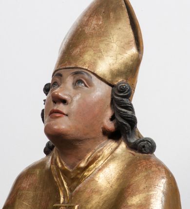 Zdjęcie nr 3: Tabernakulum w formie Arki Przymierza, adorowanej przez dwie klęczące figury starotestamentowego arcykapłana i biskupa oraz dwie stojące postacie lewitów oraz klęczące aniołów, zwieńczonej glorią promienistą z okiem Opatrzności. Wsparte na ośmiu cylindrycznych nóżkach prostopadłościenne tabernakulum jest od frontu podzielone na trzy pola wyznaczone kanelowanymi listwami. Pole środkowe stanowią drzwiczki z rytymi cyframi Dekalogu z ukrzyżowanym Chrystusem, pola boczne z wiązką pałek wodnych z jednej i winnym gronem z drugiej strony. Na skłębionych chmurach z podestem leży Baranek (obecnie w jego miejscu znajduje się figura Matki Boskiej). W tle znacznej wielkości gloria promienista z wieńcem chmur i umieszczonym w nim okiem Opatrzności oraz dwie uskrzydlone główki, nad którymi papieska tiara ze skrzyżowanymi kluczami. Po bokach Baranka dwa klęczące, uskrzydlone nagie aniołki. Obok tabernakulum dwie klęczące postacie z kadzielnicami w rękach. Postać po lewej w stroju biskupim, w albie, stule i kapie oraz infule z dwiema taśmami. Postać po prawej stronie jest ubrany w tradycyjny starotestamentowy strój – efod czyli tunikę i płaszcz wierzchni przepasany na biodrach, pektorał na piersi i zawój na głowie. Za nimi dwaj stojący lewici w tunikach przepasanych na biodrach i wysokich butach. Adorujące Baranka anioły w pozycji klęczącej z rękami skrzyżowanymi na piersi, ze skrzydłami na plecach i nogami w połowie utworzonymi ze skrzydeł.  


