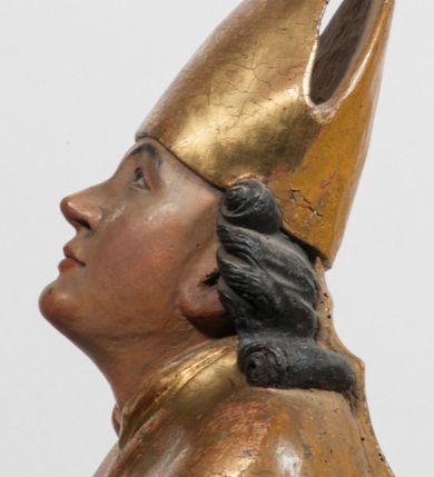 Zdjęcie nr 6: Tabernakulum w formie Arki Przymierza, adorowanej przez dwie klęczące figury starotestamentowego arcykapłana i biskupa oraz dwie stojące postacie lewitów oraz klęczące aniołów, zwieńczonej glorią promienistą z okiem Opatrzności. Wsparte na ośmiu cylindrycznych nóżkach prostopadłościenne tabernakulum jest od frontu podzielone na trzy pola wyznaczone kanelowanymi listwami. Pole środkowe stanowią drzwiczki z rytymi cyframi Dekalogu z ukrzyżowanym Chrystusem, pola boczne z wiązką pałek wodnych z jednej i winnym gronem z drugiej strony. Na skłębionych chmurach z podestem leży Baranek (obecnie w jego miejscu znajduje się figura Matki Boskiej). W tle znacznej wielkości gloria promienista z wieńcem chmur i umieszczonym w nim okiem Opatrzności oraz dwie uskrzydlone główki, nad którymi papieska tiara ze skrzyżowanymi kluczami. Po bokach Baranka dwa klęczące, uskrzydlone nagie aniołki. Obok tabernakulum dwie klęczące postacie z kadzielnicami w rękach. Postać po lewej w stroju biskupim, w albie, stule i kapie oraz infule z dwiema taśmami. Postać po prawej stronie jest ubrany w tradycyjny starotestamentowy strój – efod czyli tunikę i płaszcz wierzchni przepasany na biodrach, pektorał na piersi i zawój na głowie. Za nimi dwaj stojący lewici w tunikach przepasanych na biodrach i wysokich butach. Adorujące Baranka anioły w pozycji klęczącej z rękami skrzyżowanymi na piersi, ze skrzydłami na plecach i nogami w połowie utworzonymi ze skrzydeł.  


