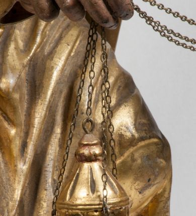 Zdjęcie nr 13: Tabernakulum w formie Arki Przymierza, adorowanej przez dwie klęczące figury starotestamentowego arcykapłana i biskupa oraz dwie stojące postacie lewitów oraz klęczące aniołów, zwieńczonej glorią promienistą z okiem Opatrzności. Wsparte na ośmiu cylindrycznych nóżkach prostopadłościenne tabernakulum jest od frontu podzielone na trzy pola wyznaczone kanelowanymi listwami. Pole środkowe stanowią drzwiczki z rytymi cyframi Dekalogu z ukrzyżowanym Chrystusem, pola boczne z wiązką pałek wodnych z jednej i winnym gronem z drugiej strony. Na skłębionych chmurach z podestem leży Baranek (obecnie w jego miejscu znajduje się figura Matki Boskiej). W tle znacznej wielkości gloria promienista z wieńcem chmur i umieszczonym w nim okiem Opatrzności oraz dwie uskrzydlone główki, nad którymi papieska tiara ze skrzyżowanymi kluczami. Po bokach Baranka dwa klęczące, uskrzydlone nagie aniołki. Obok tabernakulum dwie klęczące postacie z kadzielnicami w rękach. Postać po lewej w stroju biskupim, w albie, stule i kapie oraz infule z dwiema taśmami. Postać po prawej stronie jest ubrany w tradycyjny starotestamentowy strój – efod czyli tunikę i płaszcz wierzchni przepasany na biodrach, pektorał na piersi i zawój na głowie. Za nimi dwaj stojący lewici w tunikach przepasanych na biodrach i wysokich butach. Adorujące Baranka anioły w pozycji klęczącej z rękami skrzyżowanymi na piersi, ze skrzydłami na plecach i nogami w połowie utworzonymi ze skrzydeł.  


