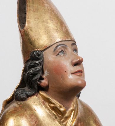 Zdjęcie nr 15: Tabernakulum w formie Arki Przymierza, adorowanej przez dwie klęczące figury starotestamentowego arcykapłana i biskupa oraz dwie stojące postacie lewitów oraz klęczące aniołów, zwieńczonej glorią promienistą z okiem Opatrzności. Wsparte na ośmiu cylindrycznych nóżkach prostopadłościenne tabernakulum jest od frontu podzielone na trzy pola wyznaczone kanelowanymi listwami. Pole środkowe stanowią drzwiczki z rytymi cyframi Dekalogu z ukrzyżowanym Chrystusem, pola boczne z wiązką pałek wodnych z jednej i winnym gronem z drugiej strony. Na skłębionych chmurach z podestem leży Baranek (obecnie w jego miejscu znajduje się figura Matki Boskiej). W tle znacznej wielkości gloria promienista z wieńcem chmur i umieszczonym w nim okiem Opatrzności oraz dwie uskrzydlone główki, nad którymi papieska tiara ze skrzyżowanymi kluczami. Po bokach Baranka dwa klęczące, uskrzydlone nagie aniołki. Obok tabernakulum dwie klęczące postacie z kadzielnicami w rękach. Postać po lewej w stroju biskupim, w albie, stule i kapie oraz infule z dwiema taśmami. Postać po prawej stronie jest ubrany w tradycyjny starotestamentowy strój – efod czyli tunikę i płaszcz wierzchni przepasany na biodrach, pektorał na piersi i zawój na głowie. Za nimi dwaj stojący lewici w tunikach przepasanych na biodrach i wysokich butach. Adorujące Baranka anioły w pozycji klęczącej z rękami skrzyżowanymi na piersi, ze skrzydłami na plecach i nogami w połowie utworzonymi ze skrzydeł.  


