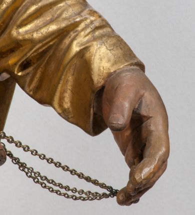 Zdjęcie nr 12: Tabernakulum w formie Arki Przymierza, adorowanej przez dwie klęczące figury starotestamentowego arcykapłana i biskupa oraz dwie stojące postacie lewitów oraz klęczące aniołów, zwieńczonej glorią promienistą z okiem Opatrzności. Wsparte na ośmiu cylindrycznych nóżkach prostopadłościenne tabernakulum jest od frontu podzielone na trzy pola wyznaczone kanelowanymi listwami. Pole środkowe stanowią drzwiczki z rytymi cyframi Dekalogu z ukrzyżowanym Chrystusem, pola boczne z wiązką pałek wodnych z jednej i winnym gronem z drugiej strony. Na skłębionych chmurach z podestem leży Baranek (obecnie w jego miejscu znajduje się figura Matki Boskiej). W tle znacznej wielkości gloria promienista z wieńcem chmur i umieszczonym w nim okiem Opatrzności oraz dwie uskrzydlone główki, nad którymi papieska tiara ze skrzyżowanymi kluczami. Po bokach Baranka dwa klęczące, uskrzydlone nagie aniołki. Obok tabernakulum dwie klęczące postacie z kadzielnicami w rękach. Postać po lewej w stroju biskupim, w albie, stule i kapie oraz infule z dwiema taśmami. Postać po prawej stronie jest ubrany w tradycyjny starotestamentowy strój – efod czyli tunikę i płaszcz wierzchni przepasany na biodrach, pektorał na piersi i zawój na głowie. Za nimi dwaj stojący lewici w tunikach przepasanych na biodrach i wysokich butach. Adorujące Baranka anioły w pozycji klęczącej z rękami skrzyżowanymi na piersi, ze skrzydłami na plecach i nogami w połowie utworzonymi ze skrzydeł.  


