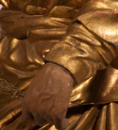 Zdjęcie nr 19: Tabernakulum w formie Arki Przymierza, adorowanej przez dwie klęczące figury starotestamentowego arcykapłana i biskupa oraz dwie stojące postacie lewitów oraz klęczące aniołów, zwieńczonej glorią promienistą z okiem Opatrzności. Wsparte na ośmiu cylindrycznych nóżkach prostopadłościenne tabernakulum jest od frontu podzielone na trzy pola wyznaczone kanelowanymi listwami. Pole środkowe stanowią drzwiczki z rytymi cyframi Dekalogu z ukrzyżowanym Chrystusem, pola boczne z wiązką pałek wodnych z jednej i winnym gronem z drugiej strony. Na skłębionych chmurach z podestem leży Baranek (obecnie w jego miejscu znajduje się figura Matki Boskiej). W tle znacznej wielkości gloria promienista z wieńcem chmur i umieszczonym w nim okiem Opatrzności oraz dwie uskrzydlone główki, nad którymi papieska tiara ze skrzyżowanymi kluczami. Po bokach Baranka dwa klęczące, uskrzydlone nagie aniołki. Obok tabernakulum dwie klęczące postacie z kadzielnicami w rękach. Postać po lewej w stroju biskupim, w albie, stule i kapie oraz infule z dwiema taśmami. Postać po prawej stronie jest ubrany w tradycyjny starotestamentowy strój – efod czyli tunikę i płaszcz wierzchni przepasany na biodrach, pektorał na piersi i zawój na głowie. Za nimi dwaj stojący lewici w tunikach przepasanych na biodrach i wysokich butach. Adorujące Baranka anioły w pozycji klęczącej z rękami skrzyżowanymi na piersi, ze skrzydłami na plecach i nogami w połowie utworzonymi ze skrzydeł.  


