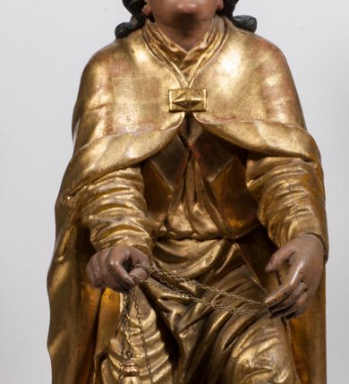 Zdjęcie nr 18: Tabernakulum w formie Arki Przymierza, adorowanej przez dwie klęczące figury starotestamentowego arcykapłana i biskupa oraz dwie stojące postacie lewitów oraz klęczące aniołów, zwieńczonej glorią promienistą z okiem Opatrzności. Wsparte na ośmiu cylindrycznych nóżkach prostopadłościenne tabernakulum jest od frontu podzielone na trzy pola wyznaczone kanelowanymi listwami. Pole środkowe stanowią drzwiczki z rytymi cyframi Dekalogu z ukrzyżowanym Chrystusem, pola boczne z wiązką pałek wodnych z jednej i winnym gronem z drugiej strony. Na skłębionych chmurach z podestem leży Baranek (obecnie w jego miejscu znajduje się figura Matki Boskiej). W tle znacznej wielkości gloria promienista z wieńcem chmur i umieszczonym w nim okiem Opatrzności oraz dwie uskrzydlone główki, nad którymi papieska tiara ze skrzyżowanymi kluczami. Po bokach Baranka dwa klęczące, uskrzydlone nagie aniołki. Obok tabernakulum dwie klęczące postacie z kadzielnicami w rękach. Postać po lewej w stroju biskupim, w albie, stule i kapie oraz infule z dwiema taśmami. Postać po prawej stronie jest ubrany w tradycyjny starotestamentowy strój – efod czyli tunikę i płaszcz wierzchni przepasany na biodrach, pektorał na piersi i zawój na głowie. Za nimi dwaj stojący lewici w tunikach przepasanych na biodrach i wysokich butach. Adorujące Baranka anioły w pozycji klęczącej z rękami skrzyżowanymi na piersi, ze skrzydłami na plecach i nogami w połowie utworzonymi ze skrzydeł.  


