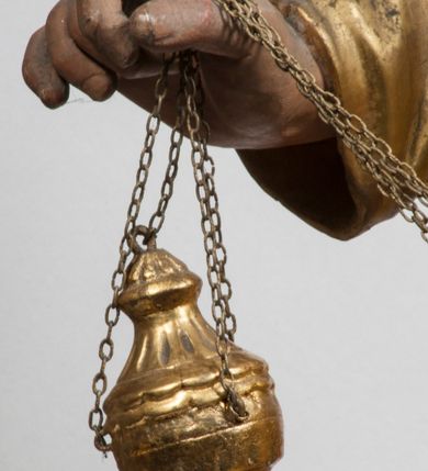Zdjęcie nr 20: Tabernakulum w formie Arki Przymierza, adorowanej przez dwie klęczące figury starotestamentowego arcykapłana i biskupa oraz dwie stojące postacie lewitów oraz klęczące aniołów, zwieńczonej glorią promienistą z okiem Opatrzności. Wsparte na ośmiu cylindrycznych nóżkach prostopadłościenne tabernakulum jest od frontu podzielone na trzy pola wyznaczone kanelowanymi listwami. Pole środkowe stanowią drzwiczki z rytymi cyframi Dekalogu z ukrzyżowanym Chrystusem, pola boczne z wiązką pałek wodnych z jednej i winnym gronem z drugiej strony. Na skłębionych chmurach z podestem leży Baranek (obecnie w jego miejscu znajduje się figura Matki Boskiej). W tle znacznej wielkości gloria promienista z wieńcem chmur i umieszczonym w nim okiem Opatrzności oraz dwie uskrzydlone główki, nad którymi papieska tiara ze skrzyżowanymi kluczami. Po bokach Baranka dwa klęczące, uskrzydlone nagie aniołki. Obok tabernakulum dwie klęczące postacie z kadzielnicami w rękach. Postać po lewej w stroju biskupim, w albie, stule i kapie oraz infule z dwiema taśmami. Postać po prawej stronie jest ubrany w tradycyjny starotestamentowy strój – efod czyli tunikę i płaszcz wierzchni przepasany na biodrach, pektorał na piersi i zawój na głowie. Za nimi dwaj stojący lewici w tunikach przepasanych na biodrach i wysokich butach. Adorujące Baranka anioły w pozycji klęczącej z rękami skrzyżowanymi na piersi, ze skrzydłami na plecach i nogami w połowie utworzonymi ze skrzydeł.  


