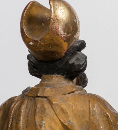 Zdjęcie nr 28: Tabernakulum w formie Arki Przymierza, adorowanej przez dwie klęczące figury starotestamentowego arcykapłana i biskupa oraz dwie stojące postacie lewitów oraz klęczące aniołów, zwieńczonej glorią promienistą z okiem Opatrzności. Wsparte na ośmiu cylindrycznych nóżkach prostopadłościenne tabernakulum jest od frontu podzielone na trzy pola wyznaczone kanelowanymi listwami. Pole środkowe stanowią drzwiczki z rytymi cyframi Dekalogu z ukrzyżowanym Chrystusem, pola boczne z wiązką pałek wodnych z jednej i winnym gronem z drugiej strony. Na skłębionych chmurach z podestem leży Baranek (obecnie w jego miejscu znajduje się figura Matki Boskiej). W tle znacznej wielkości gloria promienista z wieńcem chmur i umieszczonym w nim okiem Opatrzności oraz dwie uskrzydlone główki, nad którymi papieska tiara ze skrzyżowanymi kluczami. Po bokach Baranka dwa klęczące, uskrzydlone nagie aniołki. Obok tabernakulum dwie klęczące postacie z kadzielnicami w rękach. Postać po lewej w stroju biskupim, w albie, stule i kapie oraz infule z dwiema taśmami. Postać po prawej stronie jest ubrany w tradycyjny starotestamentowy strój – efod czyli tunikę i płaszcz wierzchni przepasany na biodrach, pektorał na piersi i zawój na głowie. Za nimi dwaj stojący lewici w tunikach przepasanych na biodrach i wysokich butach. Adorujące Baranka anioły w pozycji klęczącej z rękami skrzyżowanymi na piersi, ze skrzydłami na plecach i nogami w połowie utworzonymi ze skrzydeł.  


