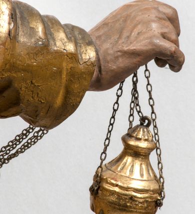 Zdjęcie nr 30: Tabernakulum w formie Arki Przymierza, adorowanej przez dwie klęczące figury starotestamentowego arcykapłana i biskupa oraz dwie stojące postacie lewitów oraz klęczące aniołów, zwieńczonej glorią promienistą z okiem Opatrzności. Wsparte na ośmiu cylindrycznych nóżkach prostopadłościenne tabernakulum jest od frontu podzielone na trzy pola wyznaczone kanelowanymi listwami. Pole środkowe stanowią drzwiczki z rytymi cyframi Dekalogu z ukrzyżowanym Chrystusem, pola boczne z wiązką pałek wodnych z jednej i winnym gronem z drugiej strony. Na skłębionych chmurach z podestem leży Baranek (obecnie w jego miejscu znajduje się figura Matki Boskiej). W tle znacznej wielkości gloria promienista z wieńcem chmur i umieszczonym w nim okiem Opatrzności oraz dwie uskrzydlone główki, nad którymi papieska tiara ze skrzyżowanymi kluczami. Po bokach Baranka dwa klęczące, uskrzydlone nagie aniołki. Obok tabernakulum dwie klęczące postacie z kadzielnicami w rękach. Postać po lewej w stroju biskupim, w albie, stule i kapie oraz infule z dwiema taśmami. Postać po prawej stronie jest ubrany w tradycyjny starotestamentowy strój – efod czyli tunikę i płaszcz wierzchni przepasany na biodrach, pektorał na piersi i zawój na głowie. Za nimi dwaj stojący lewici w tunikach przepasanych na biodrach i wysokich butach. Adorujące Baranka anioły w pozycji klęczącej z rękami skrzyżowanymi na piersi, ze skrzydłami na plecach i nogami w połowie utworzonymi ze skrzydeł.  


