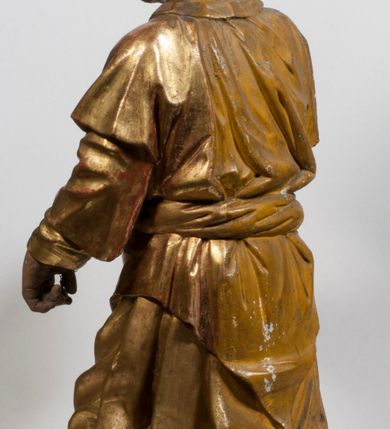 Zdjęcie nr 26: Tabernakulum w formie Arki Przymierza, adorowanej przez dwie klęczące figury starotestamentowego arcykapłana i biskupa oraz dwie stojące postacie lewitów oraz klęczące aniołów, zwieńczonej glorią promienistą z okiem Opatrzności. Wsparte na ośmiu cylindrycznych nóżkach prostopadłościenne tabernakulum jest od frontu podzielone na trzy pola wyznaczone kanelowanymi listwami. Pole środkowe stanowią drzwiczki z rytymi cyframi Dekalogu z ukrzyżowanym Chrystusem, pola boczne z wiązką pałek wodnych z jednej i winnym gronem z drugiej strony. Na skłębionych chmurach z podestem leży Baranek (obecnie w jego miejscu znajduje się figura Matki Boskiej). W tle znacznej wielkości gloria promienista z wieńcem chmur i umieszczonym w nim okiem Opatrzności oraz dwie uskrzydlone główki, nad którymi papieska tiara ze skrzyżowanymi kluczami. Po bokach Baranka dwa klęczące, uskrzydlone nagie aniołki. Obok tabernakulum dwie klęczące postacie z kadzielnicami w rękach. Postać po lewej w stroju biskupim, w albie, stule i kapie oraz infule z dwiema taśmami. Postać po prawej stronie jest ubrany w tradycyjny starotestamentowy strój – efod czyli tunikę i płaszcz wierzchni przepasany na biodrach, pektorał na piersi i zawój na głowie. Za nimi dwaj stojący lewici w tunikach przepasanych na biodrach i wysokich butach. Adorujące Baranka anioły w pozycji klęczącej z rękami skrzyżowanymi na piersi, ze skrzydłami na plecach i nogami w połowie utworzonymi ze skrzydeł.  


