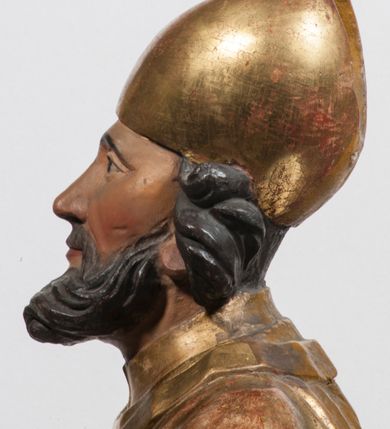 Zdjęcie nr 24: Tabernakulum w formie Arki Przymierza, adorowanej przez dwie klęczące figury starotestamentowego arcykapłana i biskupa oraz dwie stojące postacie lewitów oraz klęczące aniołów, zwieńczonej glorią promienistą z okiem Opatrzności. Wsparte na ośmiu cylindrycznych nóżkach prostopadłościenne tabernakulum jest od frontu podzielone na trzy pola wyznaczone kanelowanymi listwami. Pole środkowe stanowią drzwiczki z rytymi cyframi Dekalogu z ukrzyżowanym Chrystusem, pola boczne z wiązką pałek wodnych z jednej i winnym gronem z drugiej strony. Na skłębionych chmurach z podestem leży Baranek (obecnie w jego miejscu znajduje się figura Matki Boskiej). W tle znacznej wielkości gloria promienista z wieńcem chmur i umieszczonym w nim okiem Opatrzności oraz dwie uskrzydlone główki, nad którymi papieska tiara ze skrzyżowanymi kluczami. Po bokach Baranka dwa klęczące, uskrzydlone nagie aniołki. Obok tabernakulum dwie klęczące postacie z kadzielnicami w rękach. Postać po lewej w stroju biskupim, w albie, stule i kapie oraz infule z dwiema taśmami. Postać po prawej stronie jest ubrany w tradycyjny starotestamentowy strój – efod czyli tunikę i płaszcz wierzchni przepasany na biodrach, pektorał na piersi i zawój na głowie. Za nimi dwaj stojący lewici w tunikach przepasanych na biodrach i wysokich butach. Adorujące Baranka anioły w pozycji klęczącej z rękami skrzyżowanymi na piersi, ze skrzydłami na plecach i nogami w połowie utworzonymi ze skrzydeł.  


