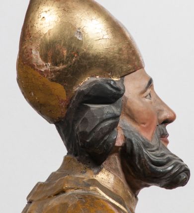 Zdjęcie nr 31: Tabernakulum w formie Arki Przymierza, adorowanej przez dwie klęczące figury starotestamentowego arcykapłana i biskupa oraz dwie stojące postacie lewitów oraz klęczące aniołów, zwieńczonej glorią promienistą z okiem Opatrzności. Wsparte na ośmiu cylindrycznych nóżkach prostopadłościenne tabernakulum jest od frontu podzielone na trzy pola wyznaczone kanelowanymi listwami. Pole środkowe stanowią drzwiczki z rytymi cyframi Dekalogu z ukrzyżowanym Chrystusem, pola boczne z wiązką pałek wodnych z jednej i winnym gronem z drugiej strony. Na skłębionych chmurach z podestem leży Baranek (obecnie w jego miejscu znajduje się figura Matki Boskiej). W tle znacznej wielkości gloria promienista z wieńcem chmur i umieszczonym w nim okiem Opatrzności oraz dwie uskrzydlone główki, nad którymi papieska tiara ze skrzyżowanymi kluczami. Po bokach Baranka dwa klęczące, uskrzydlone nagie aniołki. Obok tabernakulum dwie klęczące postacie z kadzielnicami w rękach. Postać po lewej w stroju biskupim, w albie, stule i kapie oraz infule z dwiema taśmami. Postać po prawej stronie jest ubrany w tradycyjny starotestamentowy strój – efod czyli tunikę i płaszcz wierzchni przepasany na biodrach, pektorał na piersi i zawój na głowie. Za nimi dwaj stojący lewici w tunikach przepasanych na biodrach i wysokich butach. Adorujące Baranka anioły w pozycji klęczącej z rękami skrzyżowanymi na piersi, ze skrzydłami na plecach i nogami w połowie utworzonymi ze skrzydeł.  


