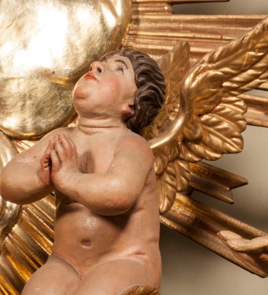 Zdjęcie nr 79: Tabernakulum w formie Arki Przymierza, adorowanej przez dwie klęczące figury starotestamentowego arcykapłana i biskupa oraz dwie stojące postacie lewitów oraz klęczące aniołów, zwieńczonej glorią promienistą z okiem Opatrzności. Wsparte na ośmiu cylindrycznych nóżkach prostopadłościenne tabernakulum jest od frontu podzielone na trzy pola wyznaczone kanelowanymi listwami. Pole środkowe stanowią drzwiczki z rytymi cyframi Dekalogu z ukrzyżowanym Chrystusem, pola boczne z wiązką pałek wodnych z jednej i winnym gronem z drugiej strony. Na skłębionych chmurach z podestem leży Baranek (obecnie w jego miejscu znajduje się figura Matki Boskiej). W tle znacznej wielkości gloria promienista z wieńcem chmur i umieszczonym w nim okiem Opatrzności oraz dwie uskrzydlone główki, nad którymi papieska tiara ze skrzyżowanymi kluczami. Po bokach Baranka dwa klęczące, uskrzydlone nagie aniołki. Obok tabernakulum dwie klęczące postacie z kadzielnicami w rękach. Postać po lewej w stroju biskupim, w albie, stule i kapie oraz infule z dwiema taśmami. Postać po prawej stronie jest ubrany w tradycyjny starotestamentowy strój – efod czyli tunikę i płaszcz wierzchni przepasany na biodrach, pektorał na piersi i zawój na głowie. Za nimi dwaj stojący lewici w tunikach przepasanych na biodrach i wysokich butach. Adorujące Baranka anioły w pozycji klęczącej z rękami skrzyżowanymi na piersi, ze skrzydłami na plecach i nogami w połowie utworzonymi ze skrzydeł.  


