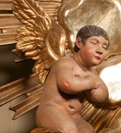 Zdjęcie nr 82: Tabernakulum w formie Arki Przymierza, adorowanej przez dwie klęczące figury starotestamentowego arcykapłana i biskupa oraz dwie stojące postacie lewitów oraz klęczące aniołów, zwieńczonej glorią promienistą z okiem Opatrzności. Wsparte na ośmiu cylindrycznych nóżkach prostopadłościenne tabernakulum jest od frontu podzielone na trzy pola wyznaczone kanelowanymi listwami. Pole środkowe stanowią drzwiczki z rytymi cyframi Dekalogu z ukrzyżowanym Chrystusem, pola boczne z wiązką pałek wodnych z jednej i winnym gronem z drugiej strony. Na skłębionych chmurach z podestem leży Baranek (obecnie w jego miejscu znajduje się figura Matki Boskiej). W tle znacznej wielkości gloria promienista z wieńcem chmur i umieszczonym w nim okiem Opatrzności oraz dwie uskrzydlone główki, nad którymi papieska tiara ze skrzyżowanymi kluczami. Po bokach Baranka dwa klęczące, uskrzydlone nagie aniołki. Obok tabernakulum dwie klęczące postacie z kadzielnicami w rękach. Postać po lewej w stroju biskupim, w albie, stule i kapie oraz infule z dwiema taśmami. Postać po prawej stronie jest ubrany w tradycyjny starotestamentowy strój – efod czyli tunikę i płaszcz wierzchni przepasany na biodrach, pektorał na piersi i zawój na głowie. Za nimi dwaj stojący lewici w tunikach przepasanych na biodrach i wysokich butach. Adorujące Baranka anioły w pozycji klęczącej z rękami skrzyżowanymi na piersi, ze skrzydłami na plecach i nogami w połowie utworzonymi ze skrzydeł.  


