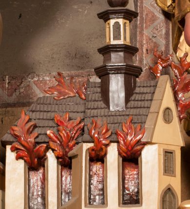 Zdjęcie nr 16: Rzeźba zwrócona w trzech czwartych w prawo, z uniesioną głową, o esowato wygiętej sylwetce, lewą nogę opiera na fragmencie płaszcza. Święty Florian w lewej uniesionej ręce trzyma drzewce rozwianej chorągwi z wizerunkiem orła w koronie, prawą wylewa z dzbana wodę na płonący budynek kościoła stojący przy jego prawej nodze. Twarz ma szczupłą, o dużych, głęboko rzeźbionych oczach, skierowanych w górę i uniesionych, zmarszczonych brwiach, dużym, lekko garbatym i zadartym nosie oraz rozchylonych ustach, okoloną krótką, silnie kręconą brodą oraz rozwianymi na boki włosami. Ubrany jest w krótką tunikę oraz zbroję torsową, przez biodra ma przewiązany pas z zawieszonym przy lewym boku mieczem. Przez lewe ramię ma zawiązany diagonalnie płaszcz, opadający na prawe przedramię oraz zawinięty na lewe udo. Na głowie ma hełm dekorowany maszkaronem z pióropuszem, a na nogach wysokie buty. Polichromia ciała naturalistyczna, włosy brązowe, strój i atrybuty złocone, detale srebrzone. 

