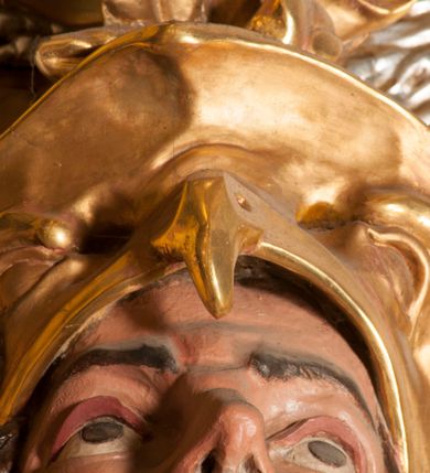 Zdjęcie nr 7: Rzeźba zwrócona w trzech czwartych w prawo, z uniesioną głową, o esowato wygiętej sylwetce, lewą nogę opiera na fragmencie płaszcza. Święty Florian w lewej uniesionej ręce trzyma drzewce rozwianej chorągwi z wizerunkiem orła w koronie, prawą wylewa z dzbana wodę na płonący budynek kościoła stojący przy jego prawej nodze. Twarz ma szczupłą, o dużych, głęboko rzeźbionych oczach, skierowanych w górę i uniesionych, zmarszczonych brwiach, dużym, lekko garbatym i zadartym nosie oraz rozchylonych ustach, okoloną krótką, silnie kręconą brodą oraz rozwianymi na boki włosami. Ubrany jest w krótką tunikę oraz zbroję torsową, przez biodra ma przewiązany pas z zawieszonym przy lewym boku mieczem. Przez lewe ramię ma zawiązany diagonalnie płaszcz, opadający na prawe przedramię oraz zawinięty na lewe udo. Na głowie ma hełm dekorowany maszkaronem z pióropuszem, a na nogach wysokie buty. Polichromia ciała naturalistyczna, włosy brązowe, strój i atrybuty złocone, detale srebrzone. 

