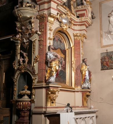 Zdjęcie nr 2: Nastawa architektoniczna, jednoosiowa, jednokondygnacyjna, ze zwieńczeniem, ustawiona na dwustrefowym cokole z wyodrębnionymi prostopadłościanami i konsolami. Ołtarz kamienny, prostopadłościenny, z kamienną mensą z portatylem. Antepedium kamienne, ujęte opaską, z rzeźbionymi maswerkami w polu. Nastawa flankowana parą opilastrowanych filarów, o kanelowanych trzonach i kapitelach kompozytowych, ustawionych pod kątem na zewnątrz, dekorowanych kwiatowymi zwisami, dźwigających pełne belkowanie wyłamane na ich osi oraz fragmenty falistego, przerwanego przyczółka z figurami aniołów. Na tle filarów ustawione figury św. Piotra i św. Pawła. Niemal całe pole główne wypełnione wnęką w formie stojącego prostokąta zamkniętego łukiem półkolistym nadwieszonym ujętą profilowaną ramą dekorowaną rocaille&#039;m, z mniejszym obrazem Rodziny Marii ze św. Janem Chrzcicielem, w osobnej, profilowanej ramie. Nad nim, w partii belkowania rocaille&#039;owy kartusz z napisem „REGNI / ET PROTECTORIBUS”. Zwieńczenie w formie leżącego prostokąta zamkniętego fragmentem falistego gzymsu. W polu obraz św. Jacka i bł. Czesława w kształcie trapezu o wklęsłych bokach, zamkniętego łukiem segmentowym nadwieszonym, ujęty ramą; flankowany dwiema parami uskrzydlonych główek anielskich. Zwieńczenie zamknięte medalionem z napisem „CHRISTI / FAMILIAE” w otoku z obłoków i uskrzydlonych główek anielskich, w glorii promienistej. Nastawa polichromowana w kolorze beżowym z detalami malowanymi na sposób imitujący jasnoróżowy marmur, ornamentyka i profile złocone. 
