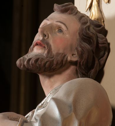 Zdjęcie nr 9: Rzeźba drążona z tyłu, ustawiona na niskiej podstawie. Figura ukazana frontalnie, z uniesioną głową, skierowaną w lewo, w kontrapoście, o esowato wygiętej sylwetce. Prawą dłoń z kluczami wyciąga w bok, lewą kładzie na piersi. Twarz pociągła o migdałowatych, blisko siebie umieszczonych oczach, lekko garbatym nosie i wąskich, rozchylonych ustach. Okolona jest krótką brodą oraz brązowymi, kręconymi włosami. Piotr ubrany jest w srebrzoną tunikę, przepasaną w talii, z kołnierzykiem oraz płaszcz przepasany w partii nóg, zawiązany na lewym biodrze, złocony o czerwonej podszewce. Polichromia ciała naturalistyczna. 
