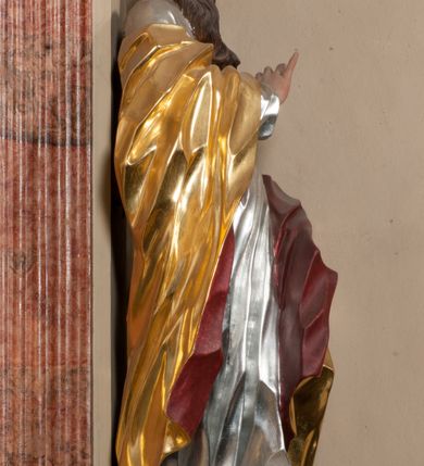 Zdjęcie nr 2: Figura drążona z tyłu, ustawiona na nieregularnej podstawie. Święty zwrócony frontalnie, z głową skierowaną w prawo, w kontrapoście, o esowato wygiętej sylwetce. W lewej, wyciągniętej w bok ręce trzyma miecz skierowany ostrzem w dół, prawą, ugiętą, unosi na tle piersi. Twarz ma pociągłą, o migdałowatych, blisko siebie osadzonych oczach, lekko garbatym nosie oraz pełnych, rozchylonych ustach. Okolona jest długą, falowaną brodą, opadającą na pierś oraz krótkimi, kręconymi, brązowymi włosami. Ubrany jest w srebrzoną tunikę, przepasaną w talii oraz złocony płaszcz z czerwoną podszewką, zarzucony na prawe ramię i opadający na lewa nogę. Polichromia ciała naturalistyczna.

