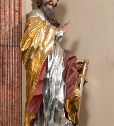 Zdjęcie nr 3: Figura drążona z tyłu, ustawiona na nieregularnej podstawie. Święty zwrócony frontalnie, z głową skierowaną w prawo, w kontrapoście, o esowato wygiętej sylwetce. W lewej, wyciągniętej w bok ręce trzyma miecz skierowany ostrzem w dół, prawą, ugiętą, unosi na tle piersi. Twarz ma pociągłą, o migdałowatych, blisko siebie osadzonych oczach, lekko garbatym nosie oraz pełnych, rozchylonych ustach. Okolona jest długą, falowaną brodą, opadającą na pierś oraz krótkimi, kręconymi, brązowymi włosami. Ubrany jest w srebrzoną tunikę, przepasaną w talii oraz złocony płaszcz z czerwoną podszewką, zarzucony na prawe ramię i opadający na lewa nogę. Polichromia ciała naturalistyczna.


