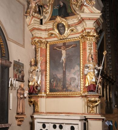 Zdjęcie nr 2: Nastawa architektoniczna, jednoosiowa, jednokondygnacyjna, ze zwieńczeniem, ustawiona na dwustrefowym cokole z wyodrębnionymi prostopadłościanami i konsolami. Ołtarz kamienny, prostopadłościenny, z kamienną mensą. Antepedium kamienne, ujęte opaską, podzielone dwoma kolumienkami na cokołach na trzy pola, każde wypełnione płaskorzeźbionymi kwiatami i prześwitami. Nastawa flankowana parą opilastrowanych filarów, o kanelowanych trzonach o kapitelach kompozytowych, ustawionych pod kątem na zewnątrz, dekorowanych kwiatowymi zwisami, dźwigających pełne belkowanie wyłamane na ich osi oraz fragmenty falistego, przerwanego przyczółka z figurami aniołów. Na tle filarów ustawione figury św. Stanisława i św. Wojciecha. Całe pole główne wypełnione wnęką w formie stojącego prostokąta ujętego ramą dekorowaną ornamentem geometrycznym, z obrazem Ukrzyżowania. Nad nim, w partii belkowania wolutowy kartusz z napisem „PA=/TRO=/NO”. Zwieńczenie w formie leżącego prostokąta zamkniętego fragmentem falistego gzymsu. W polu obraz św. Kingi w kształcie trapezu o wklęsłych bokach, zamkniętego łukiem segmentowym nadwieszonym, ujęty ramą; flankowany dwiema uskrzydlonymi główkami anielskimi. Zwieńczenie zamknięte wolutowym kartuszem przeplatanym tkaniną z napisem „RE=GNI”. Nastawa polichromowana w kolorze beżowym z detalami malowanymi na sposób imitujący jasnoróżowy marmur, ornamentyka i profile złocone. 
