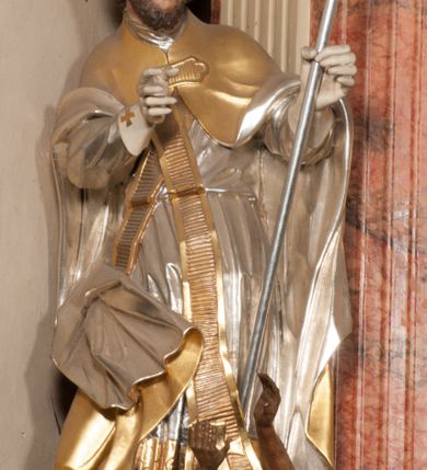 Zdjęcie nr 3: Święty zwrócony w trzech czwartych w lewo, o esowato wygiętej sylwetce. W lewej, ugiętej ręce trzyma pastorał, prawą wyciąga przed siebie. Twarz ma owalną, o okrągłych, półprzymkniętych oczach, uniesionych brwiach, lekko garbatym nosie i pełnych ustach o drążonych kącikach. Twarz ma okoloną krótką, kręconą brodą oraz silnie kręconymi, brązowymi włosami. Ubrany jest w czerwoną albę, srebrzoną rokietę o złoconej koronce przy brzegu oraz skrzyżowaną na piersi, złoconą stułę, przepasane w talii. Na ramiona ma narzuconą złoconą kapę ze srebrzoną podszewką, zapiętą klamrą na piersi, zawiniętą na prawej nodze. Na głowie ma złoconą infułę, na dłoniach białe rękawiczki. Po lewej stronie, u stóp św. Stanisława półpostać Piotrowina ukazanego tyłem do widza, unoszącego ręce w stronę świętego, z bandaną na głowie i piersiach. Polichromia w partiach ciała naturalistyczna. 



