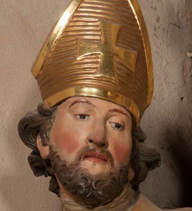 Zdjęcie nr 6: Święty zwrócony w trzech czwartych w lewo, o esowato wygiętej sylwetce. W lewej, ugiętej ręce trzyma pastorał, prawą wyciąga przed siebie. Twarz ma owalną, o okrągłych, półprzymkniętych oczach, uniesionych brwiach, lekko garbatym nosie i pełnych ustach o drążonych kącikach. Twarz ma okoloną krótką, kręconą brodą oraz silnie kręconymi, brązowymi włosami. Ubrany jest w czerwoną albę, srebrzoną rokietę o złoconej koronce przy brzegu oraz skrzyżowaną na piersi, złoconą stułę, przepasane w talii. Na ramiona ma narzuconą złoconą kapę ze srebrzoną podszewką, zapiętą klamrą na piersi, zawiniętą na prawej nodze. Na głowie ma złoconą infułę, na dłoniach białe rękawiczki. Po lewej stronie, u stóp św. Stanisława półpostać Piotrowina ukazanego tyłem do widza, unoszącego ręce w stronę świętego, z bandaną na głowie i piersiach. Polichromia w partiach ciała naturalistyczna. 



